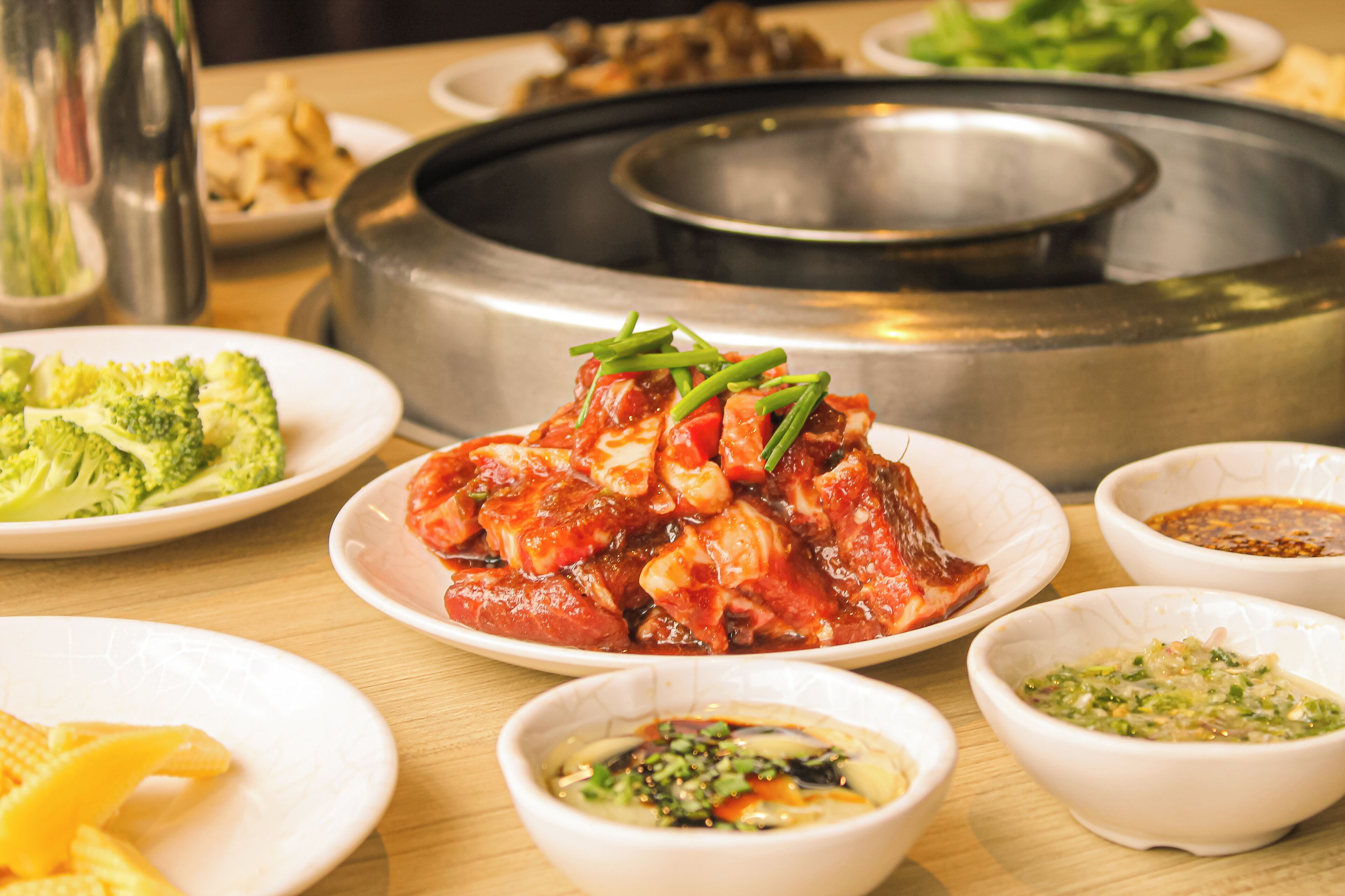 A dining table with various dishes, including a central dish of meat with vegetables, surrounded by smaller bowls of sauces and side dishes.