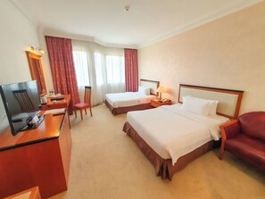 A hotel room with two beds, a desk with a TV, a chair, and a lamp. - Parkview Hotel (Jerudong)