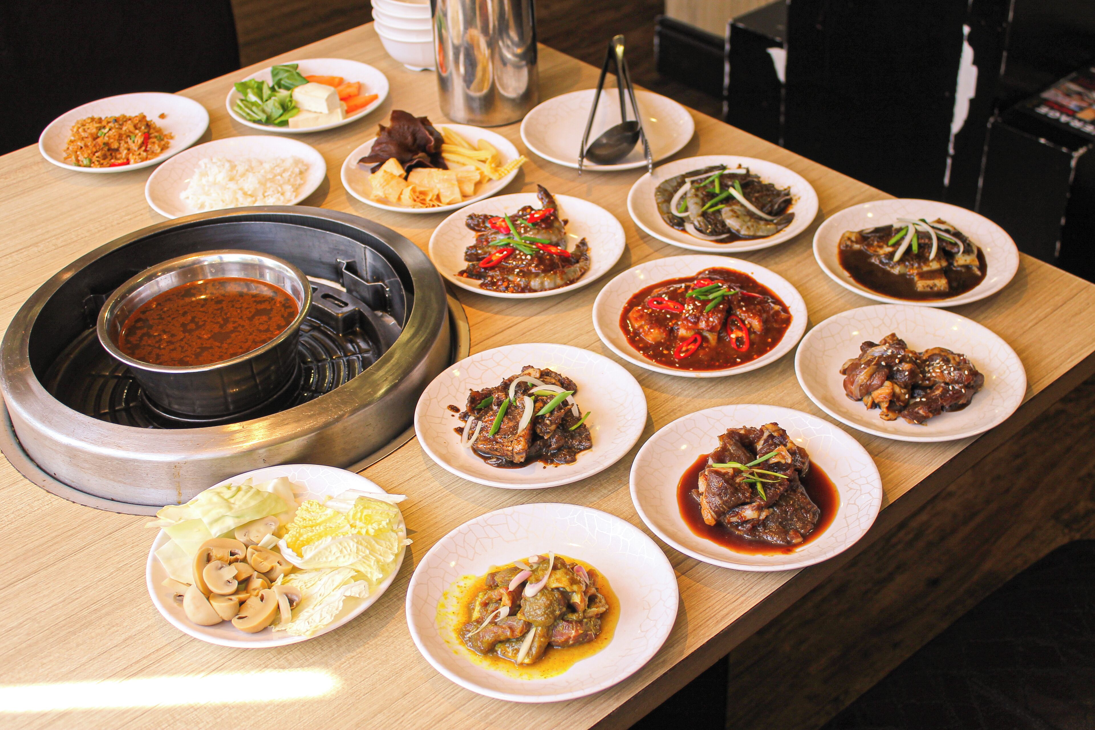 A variety of dishes on a wooden table, including a hot pot and several plates of food.