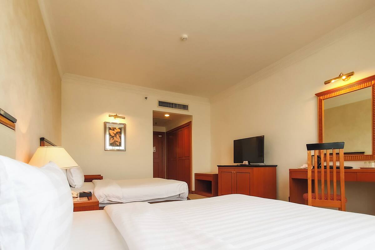 Habitación de hotel con dos camas, un escritorio, televisor, espejo y puerta que da a un baño.