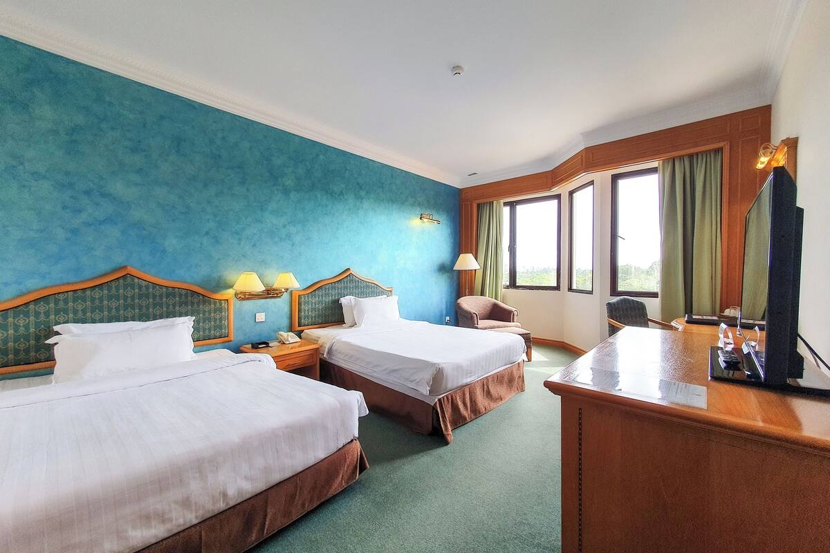 Habitación de hotel con dos camas, un escritorio, una silla, una lámpara y un ventanal grande.
