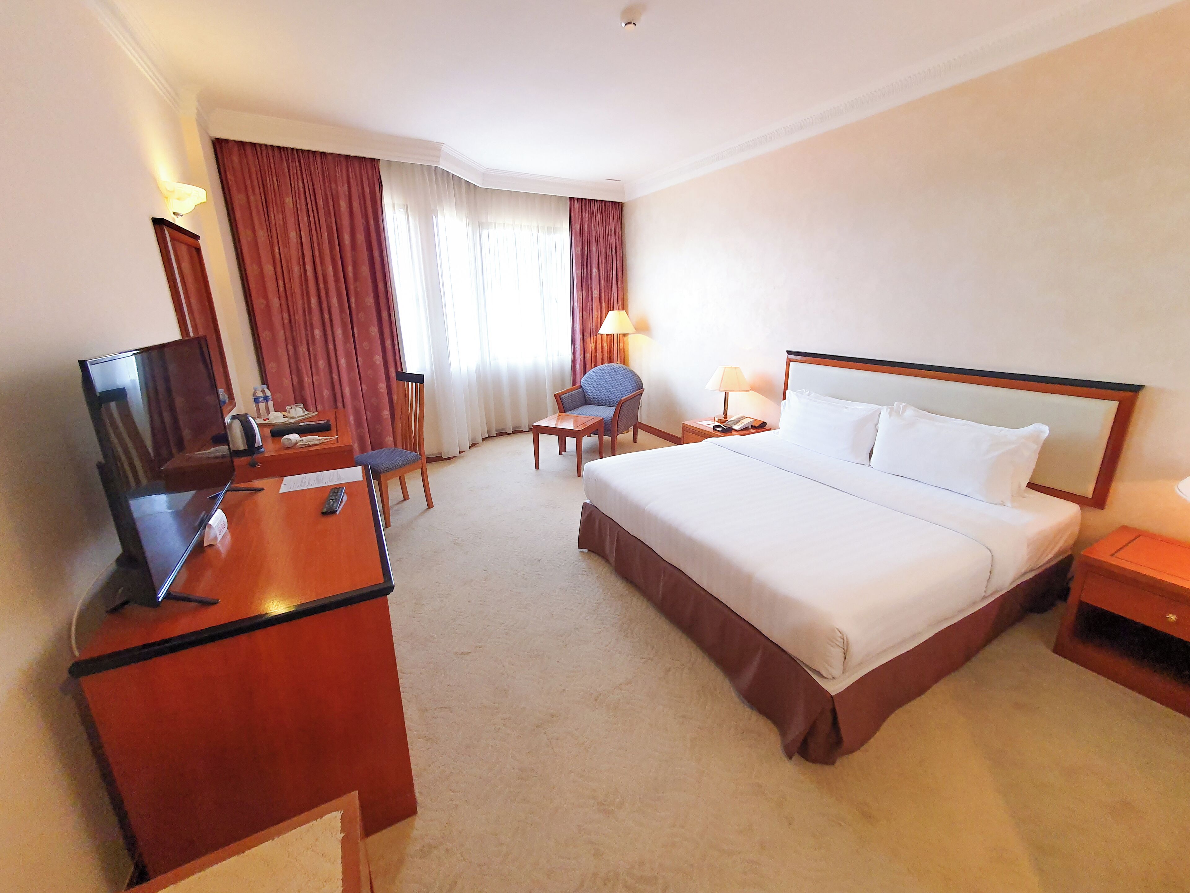 A hotel room with a bed, a desk with a television, a chair, a lamp, and a nightstand.