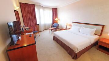 A hotel room with a bed, a desk with a television, a chair, a lamp, and a nightstand.