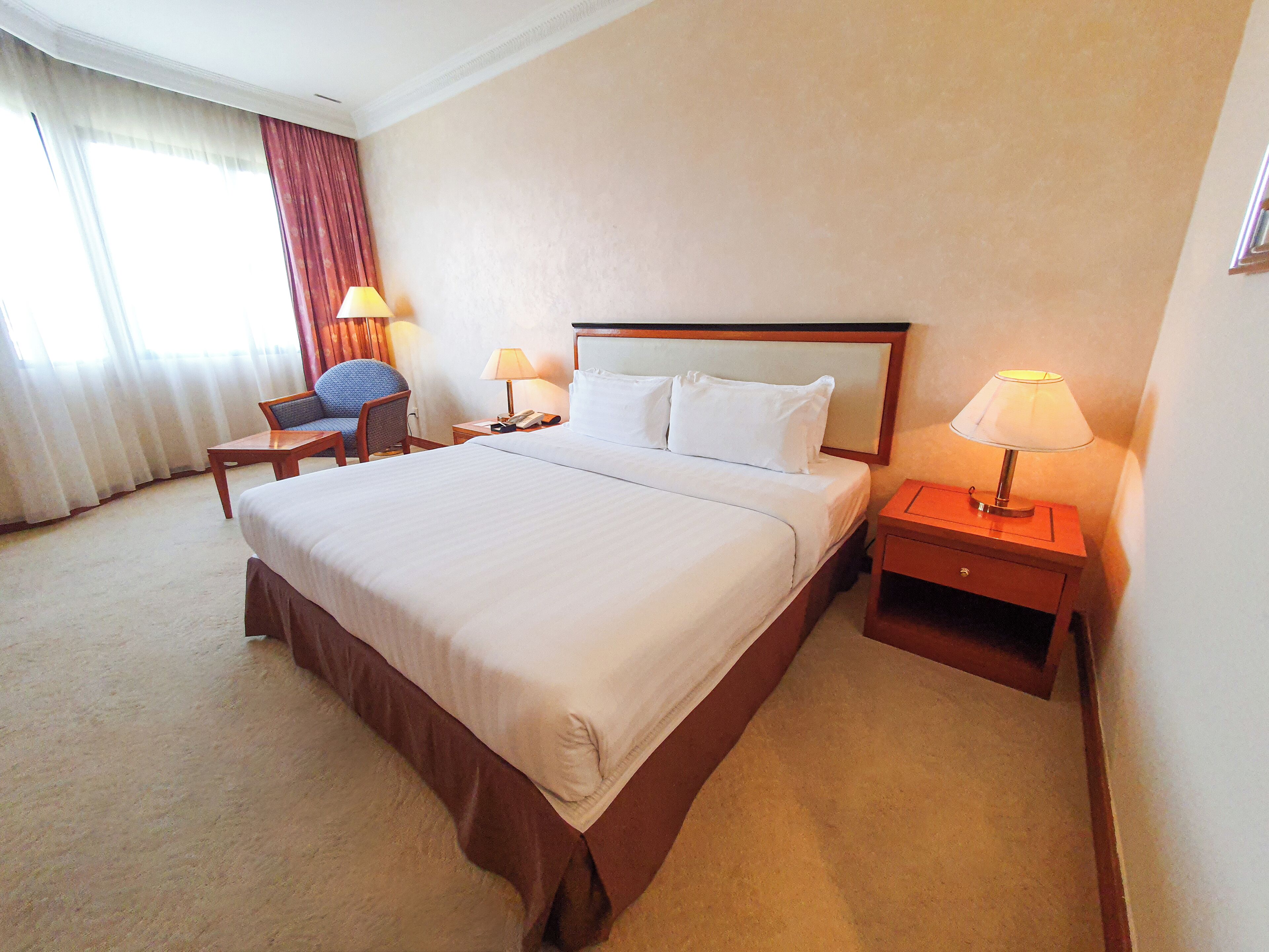 Una habitación de hotel con una cama grande, dos mesitas de noche con lámparas, una silla y un escritorio.