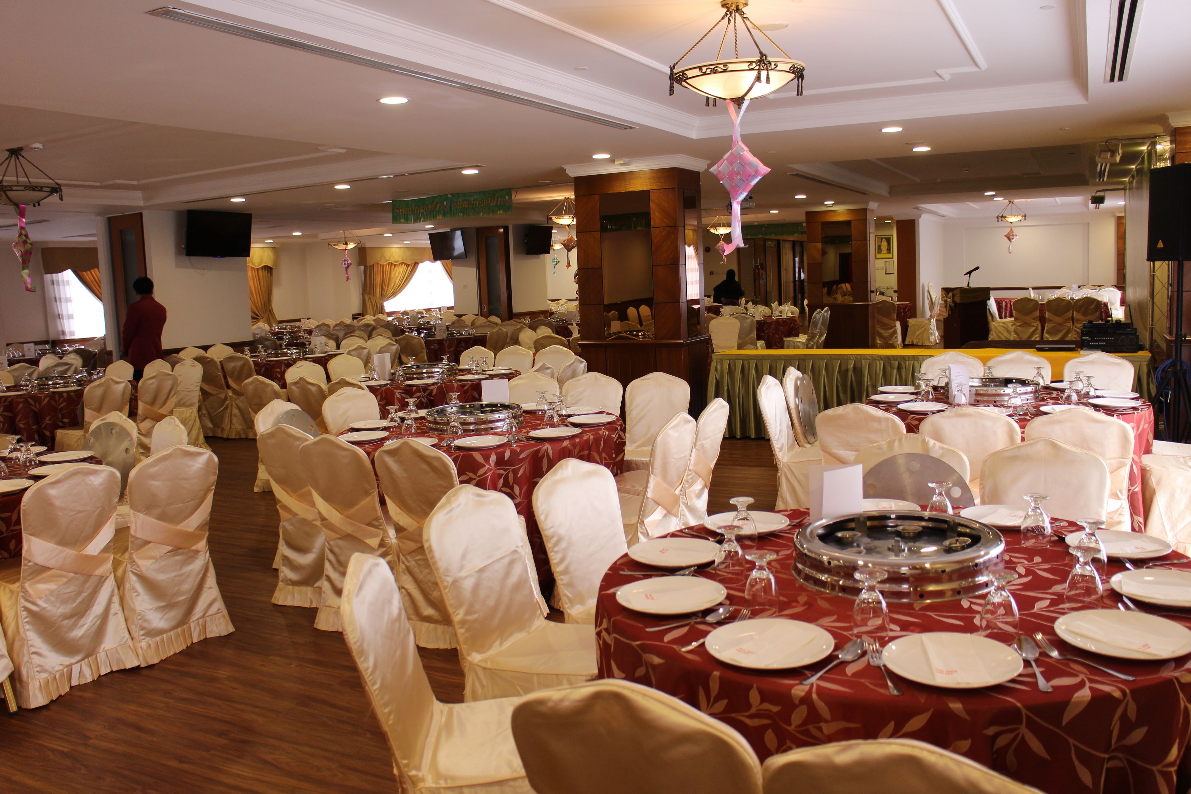 A banquet hall with round tables set for dining, each with white chairs and red tablecloths.