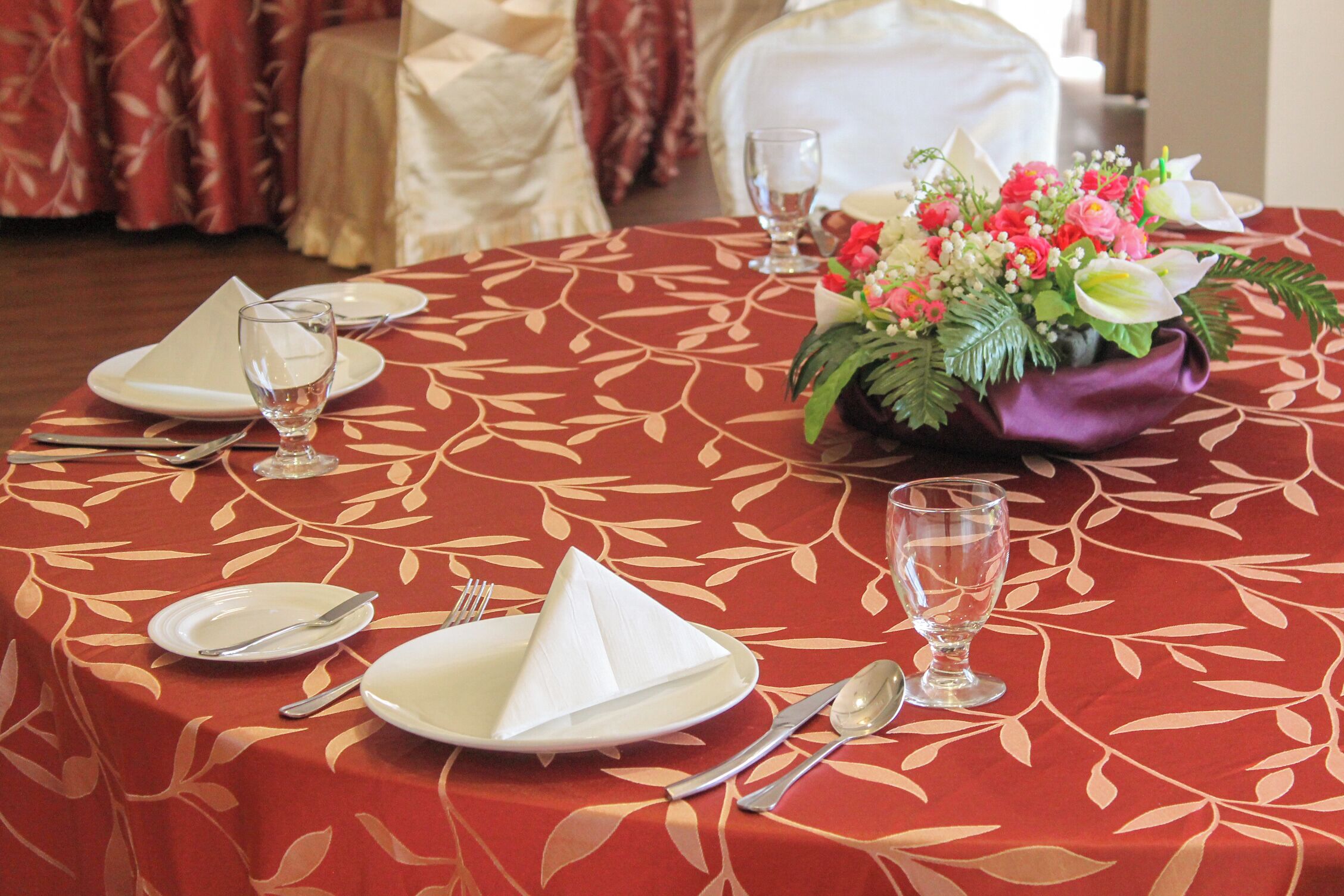 Mesa posta para quatro pessoas, com toalha vermelha, guardanapos brancos e um arranjo floral.