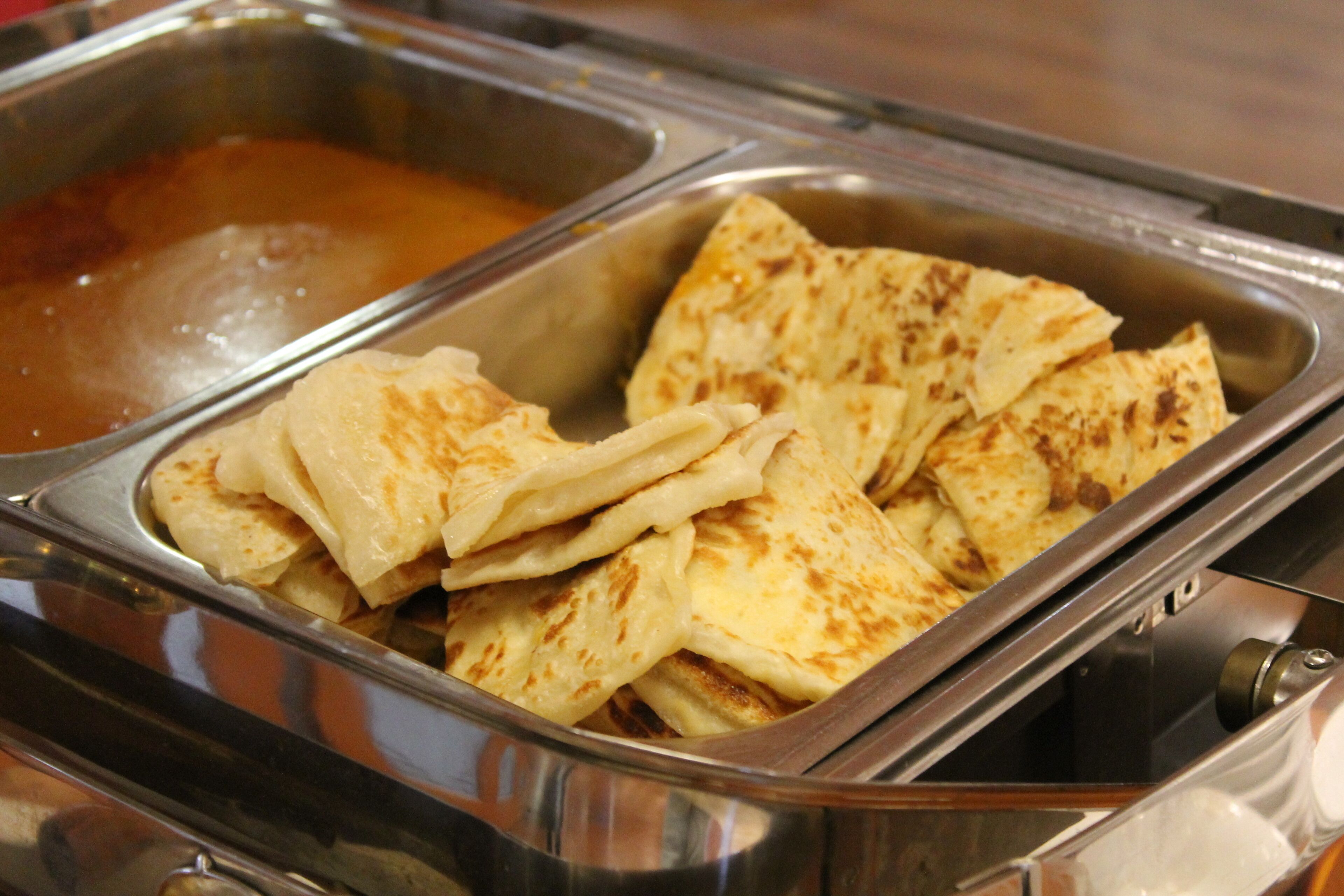A buffet with a variety of food items, including a dish with golden-brown, crispy flatbreads and a container of a brown sauce.