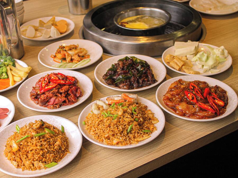 A variety of dishes including fried rice, vegetables, and seafood on a wooden table.