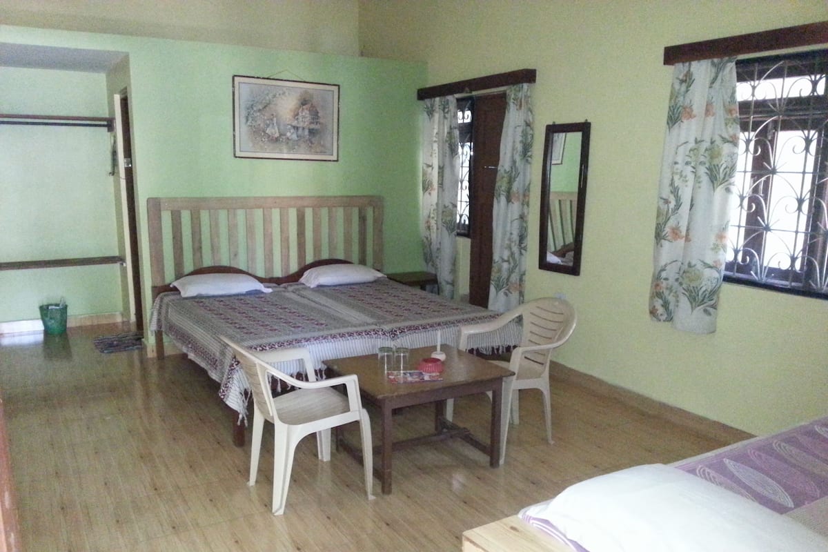 A room with a bed, a table with chairs, a window with curtains, and a wall-mounted picture.