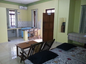 A room with a dining table and chairs, a bed with patterned bedding, a kitchen area with a counter and cabinets, and a door with a sign indicating check-out time. - Albenjoh Guesthouse (Calangute)