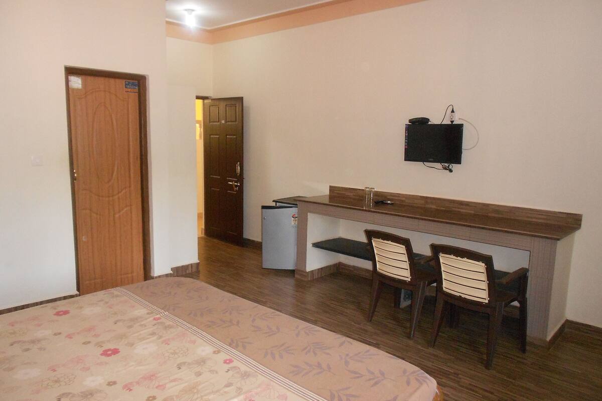 A bedroom with a bed, a desk, two chairs, a television, and a door.