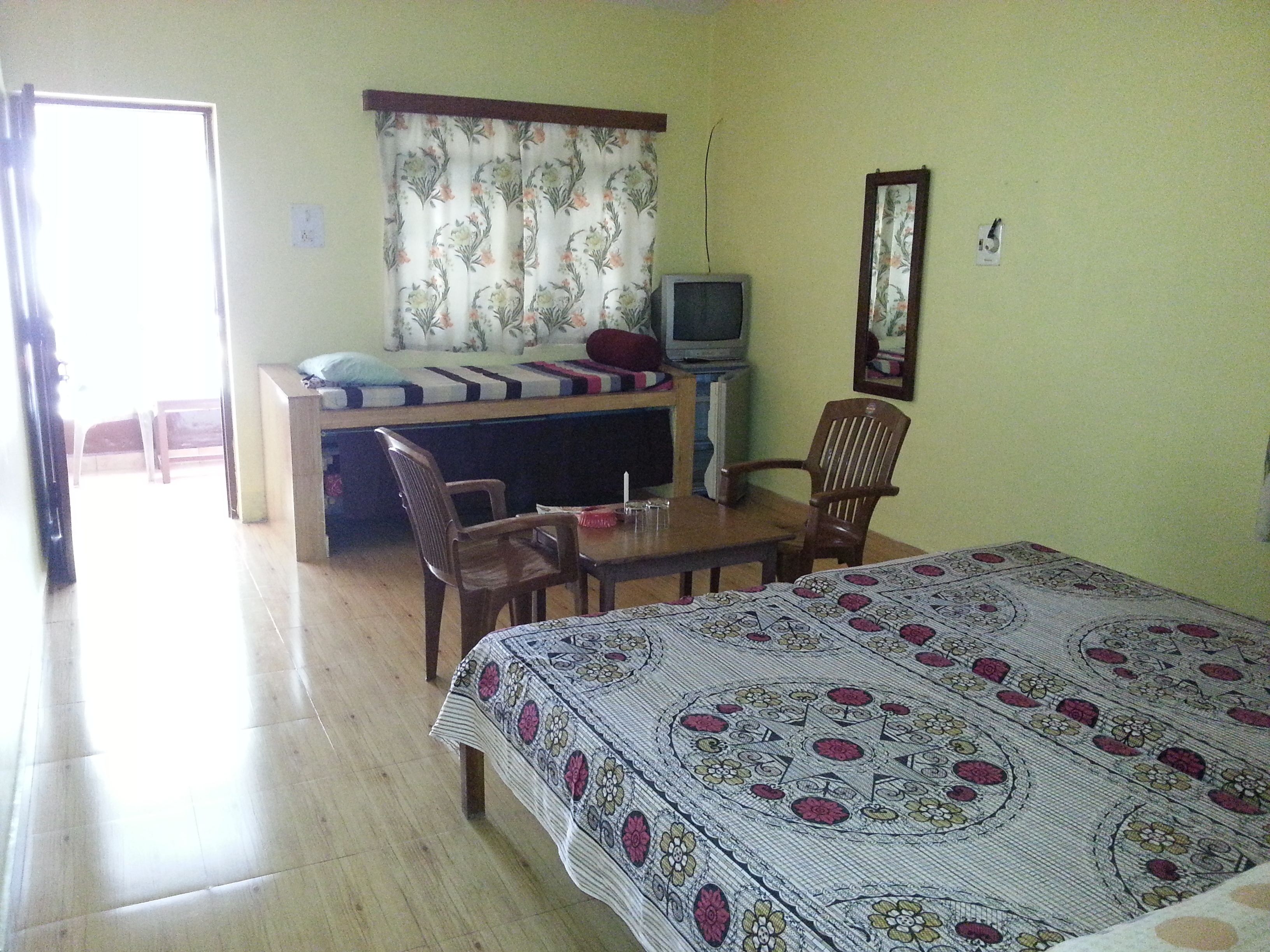 A room with a bed, a desk with a television, a chair, and a window with curtains.