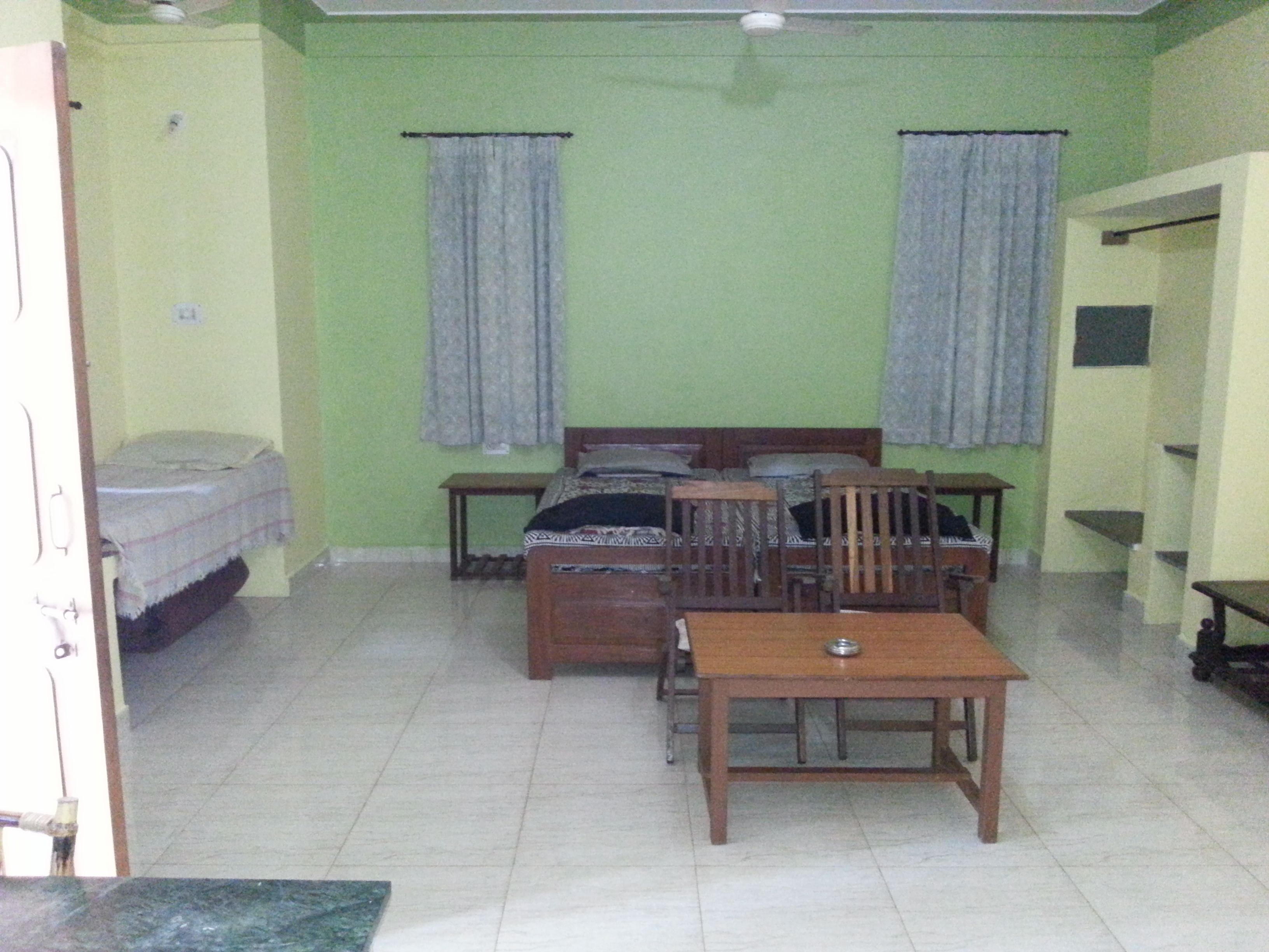 A room with a bed, two chairs, a table, and a small table with a bowl.