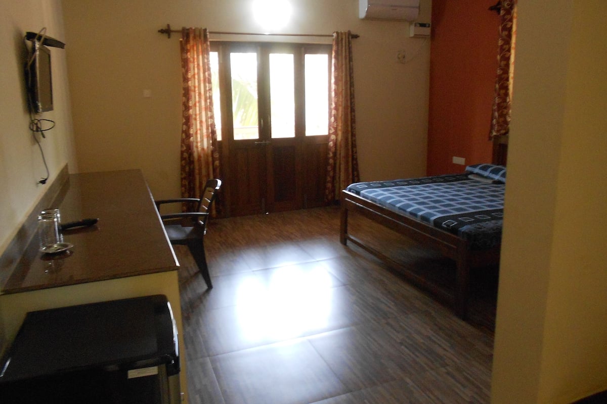 A small, well-lit room with a bed, a desk, and a chair.