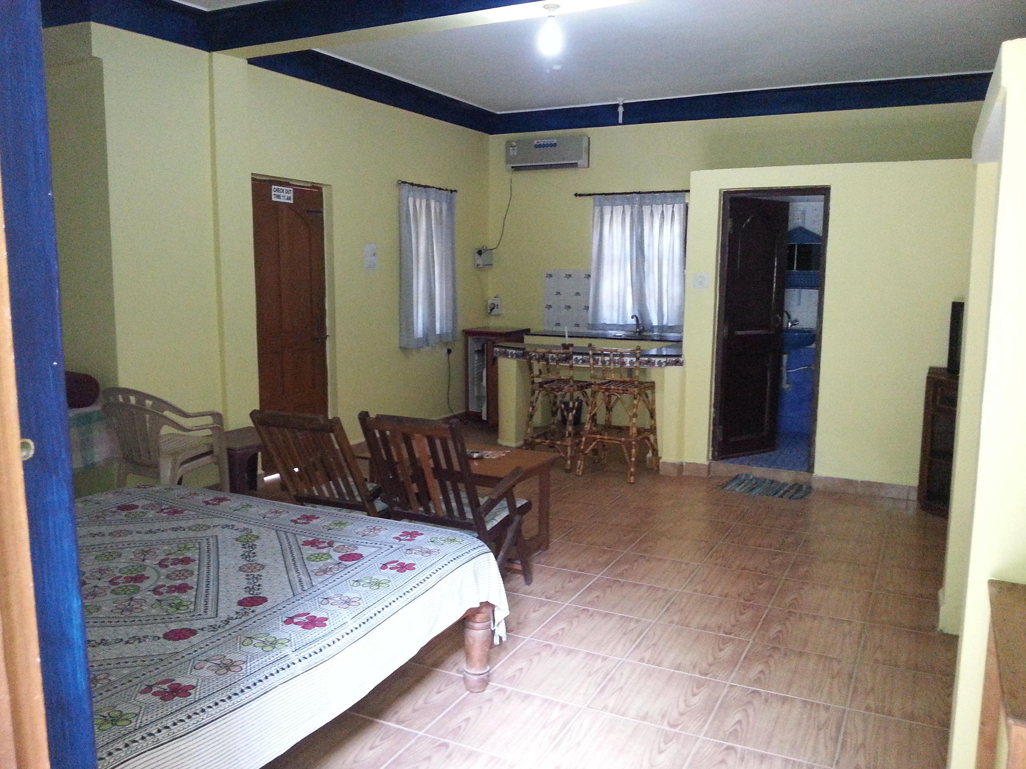 A room with a bed, a dining table with chairs, a kitchen area, and a door leading to another room.