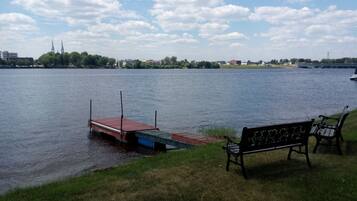 A lakeside view with a dock, a bench, and buildings in the background.