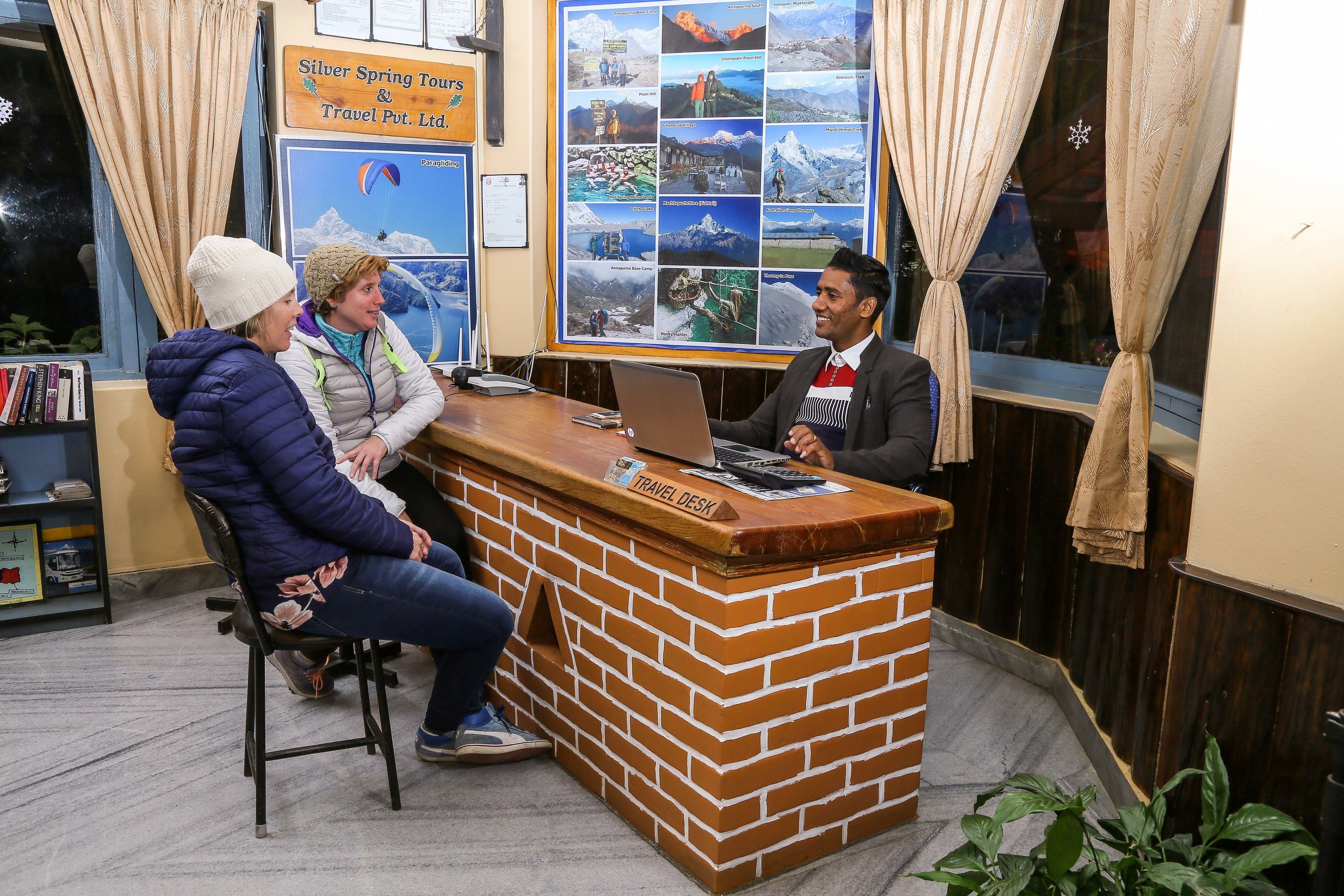 A travel desk with a laptop, a wooden counter, and a bulletin board with travel photos.