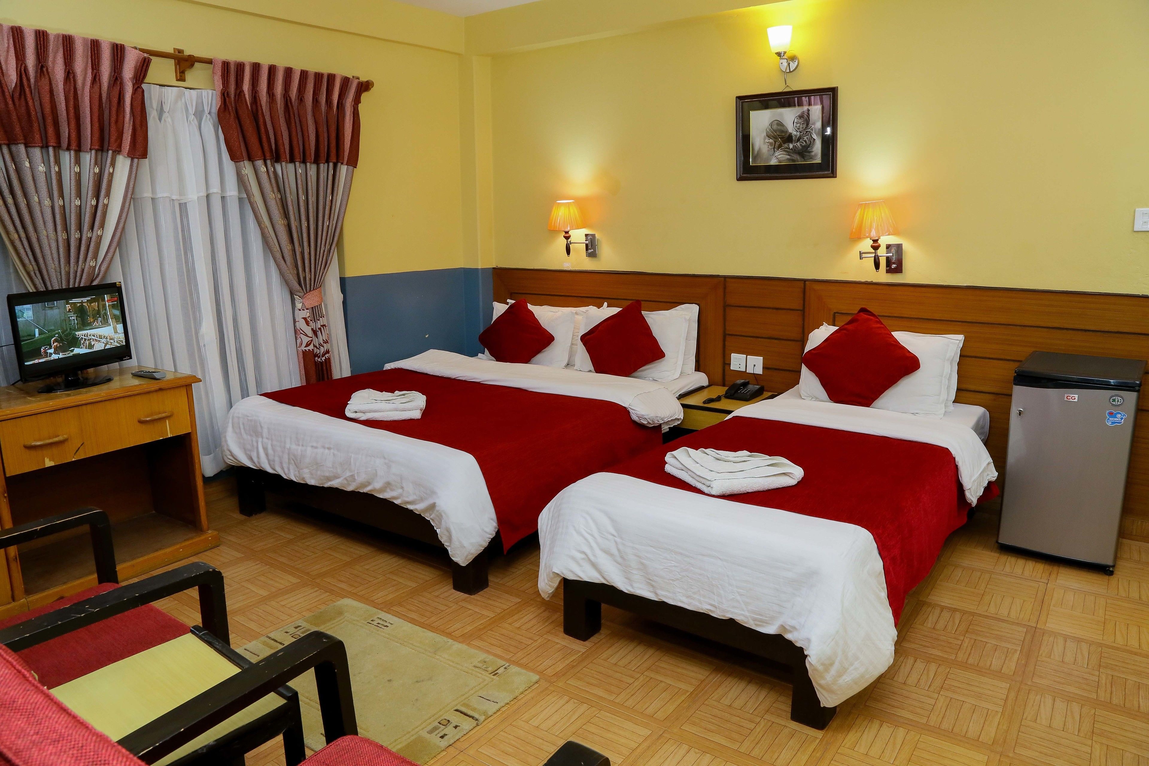A hotel room with two beds, a desk, a television, and a refrigerator.