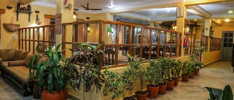 Un vestíbulo amplio con zona de estar central, varias plantas en macetas y una barandilla de madera.