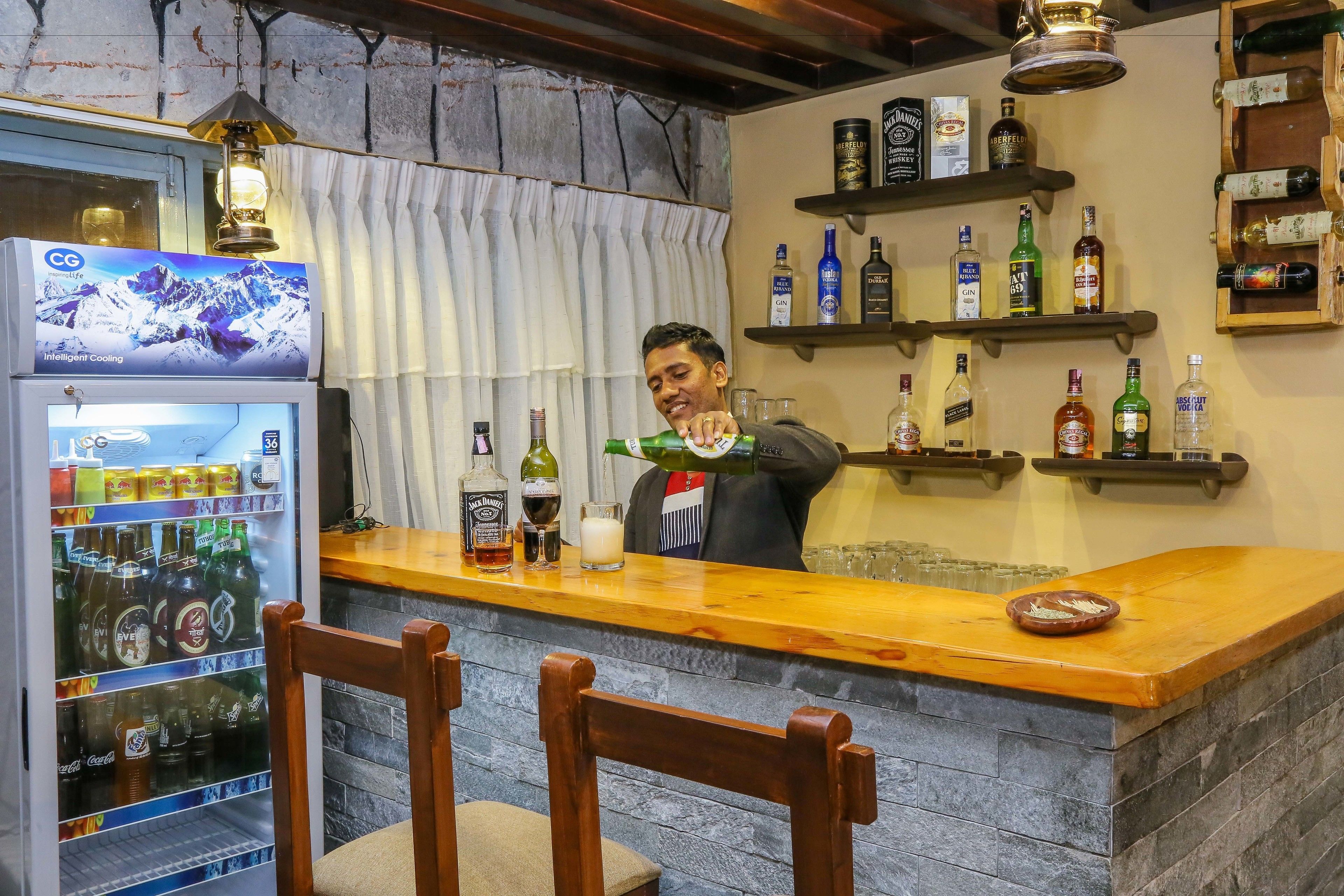 Zona de bar con un refrigerador lleno de bebidas, estantes con botellas de licor y una barra.
