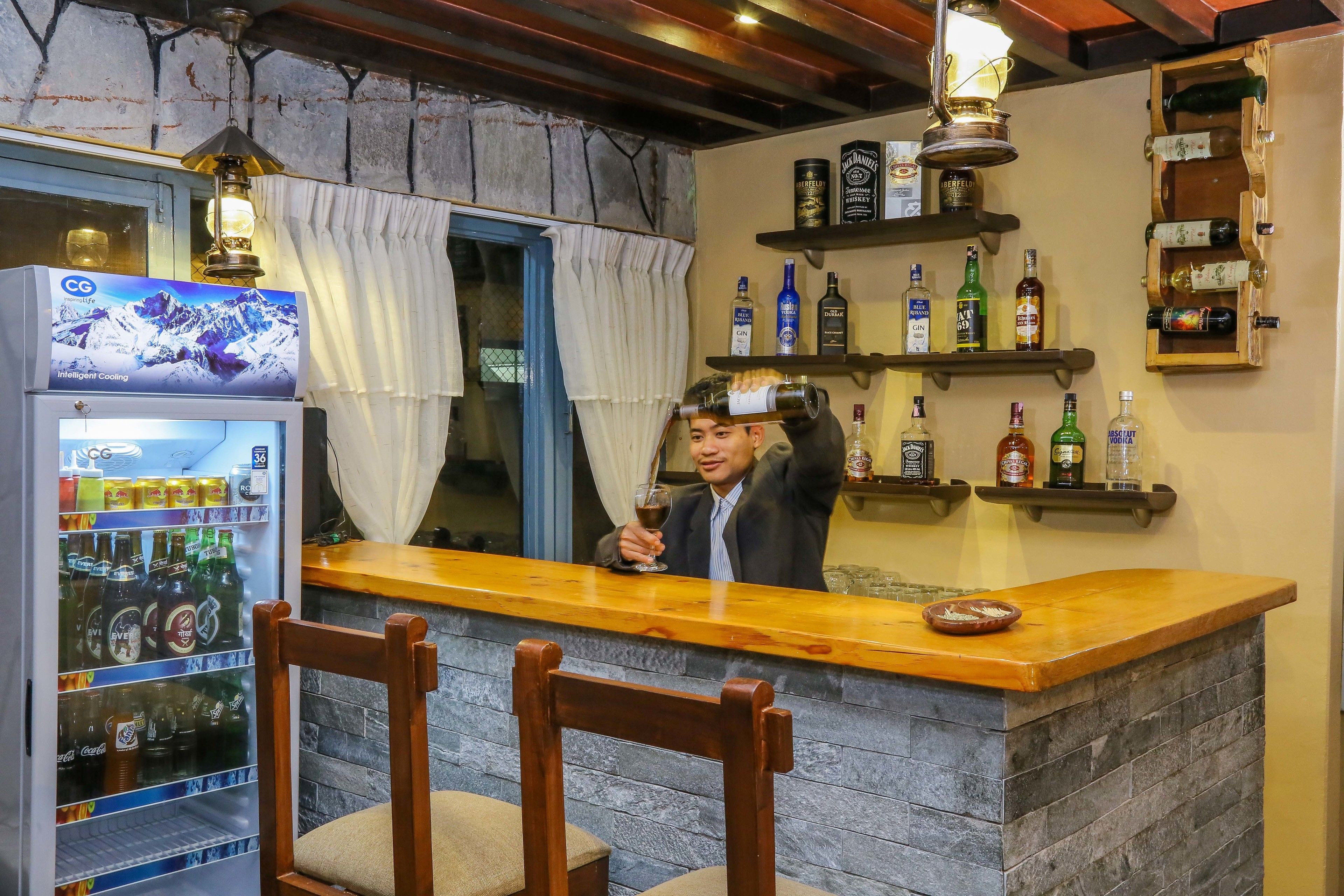 A bar area with a wooden counter, a refrigerator stocked with beverages, and shelves with bottles.