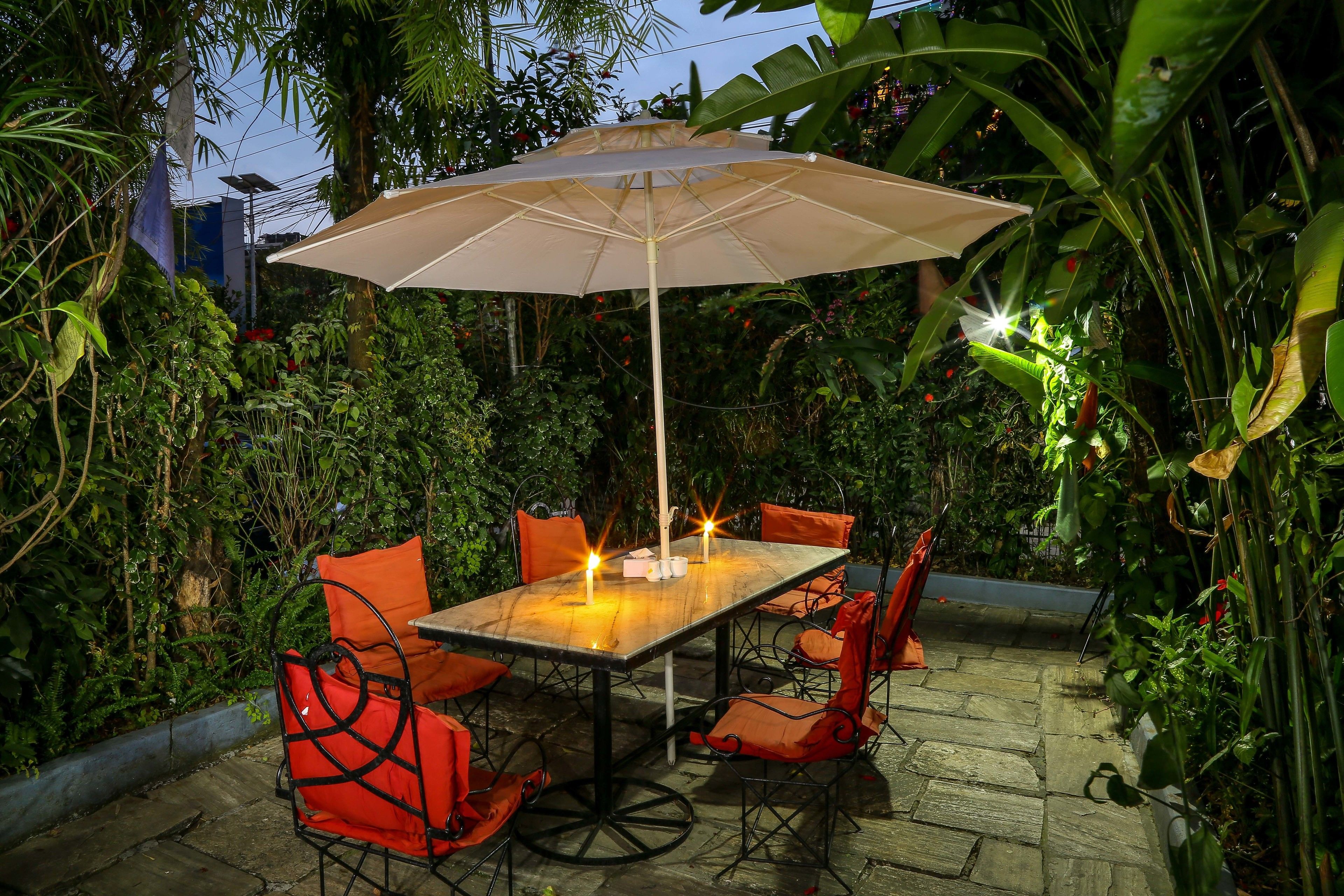An outdoor patio with a table and chairs, surrounded by lush greenery.