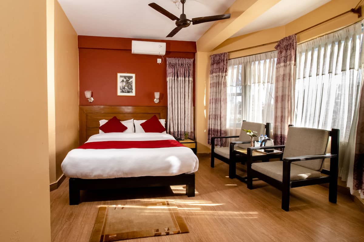 A hotel room with a bed, a desk with a chair, a ceiling fan, and curtains.