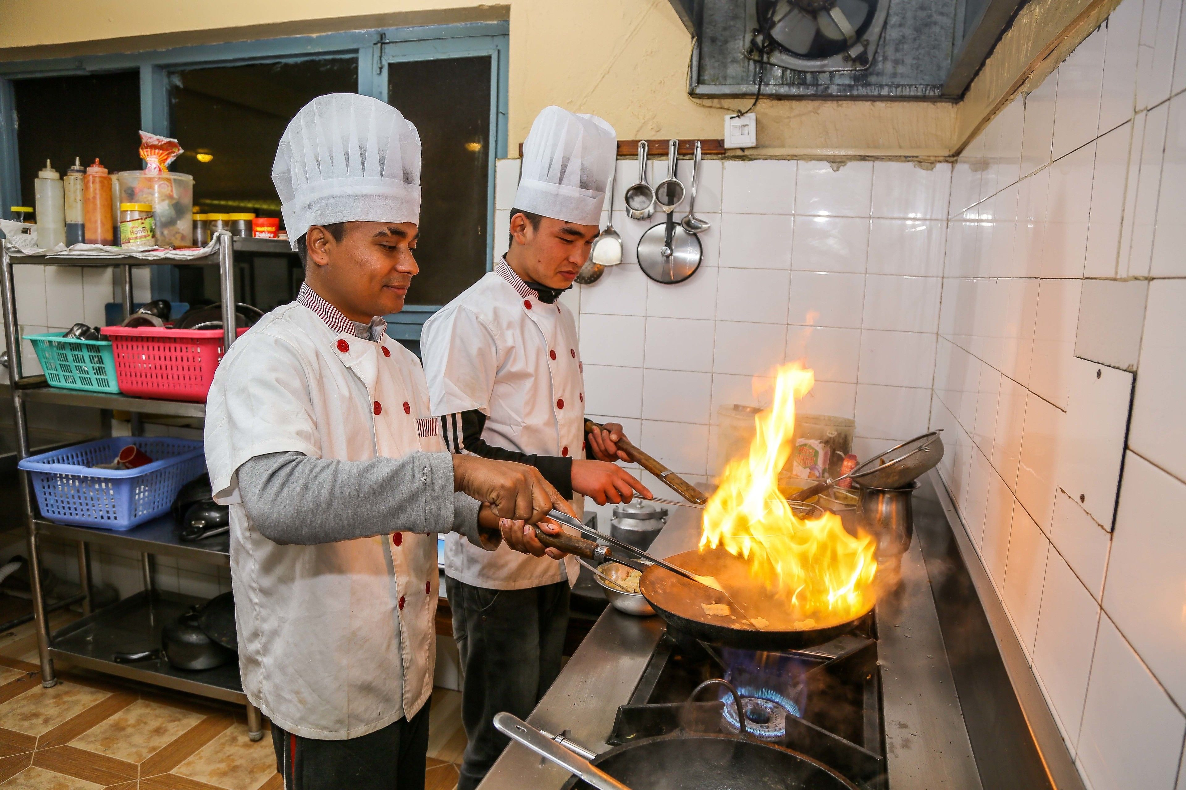 Dos cocineros cocinando con una llama grande sobre un fogón en una cocina.
