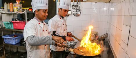 Dos cocineros cocinando con una llama grande sobre un fogón en una cocina.
