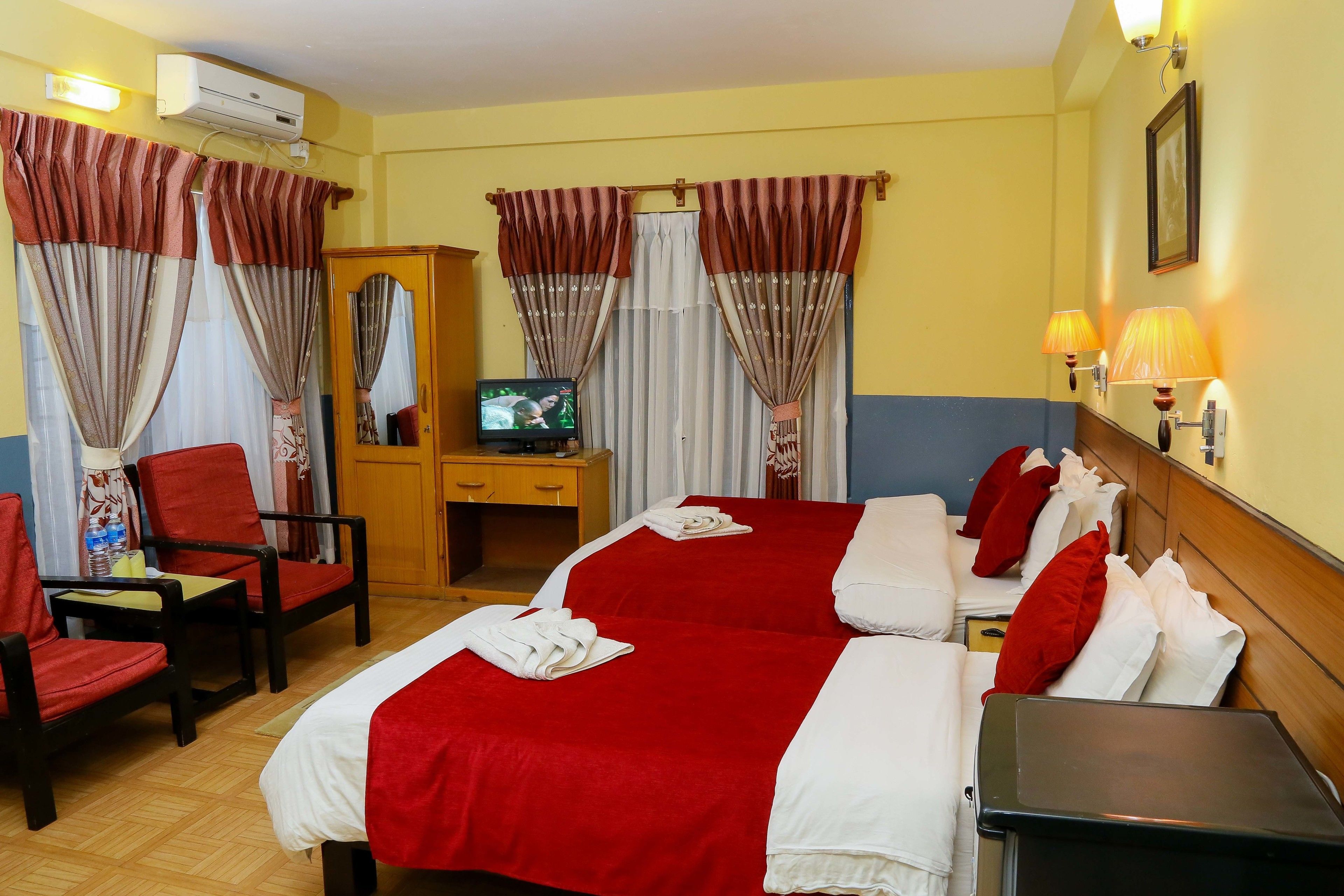 A hotel room with two beds, a desk, a TV, and a wardrobe.