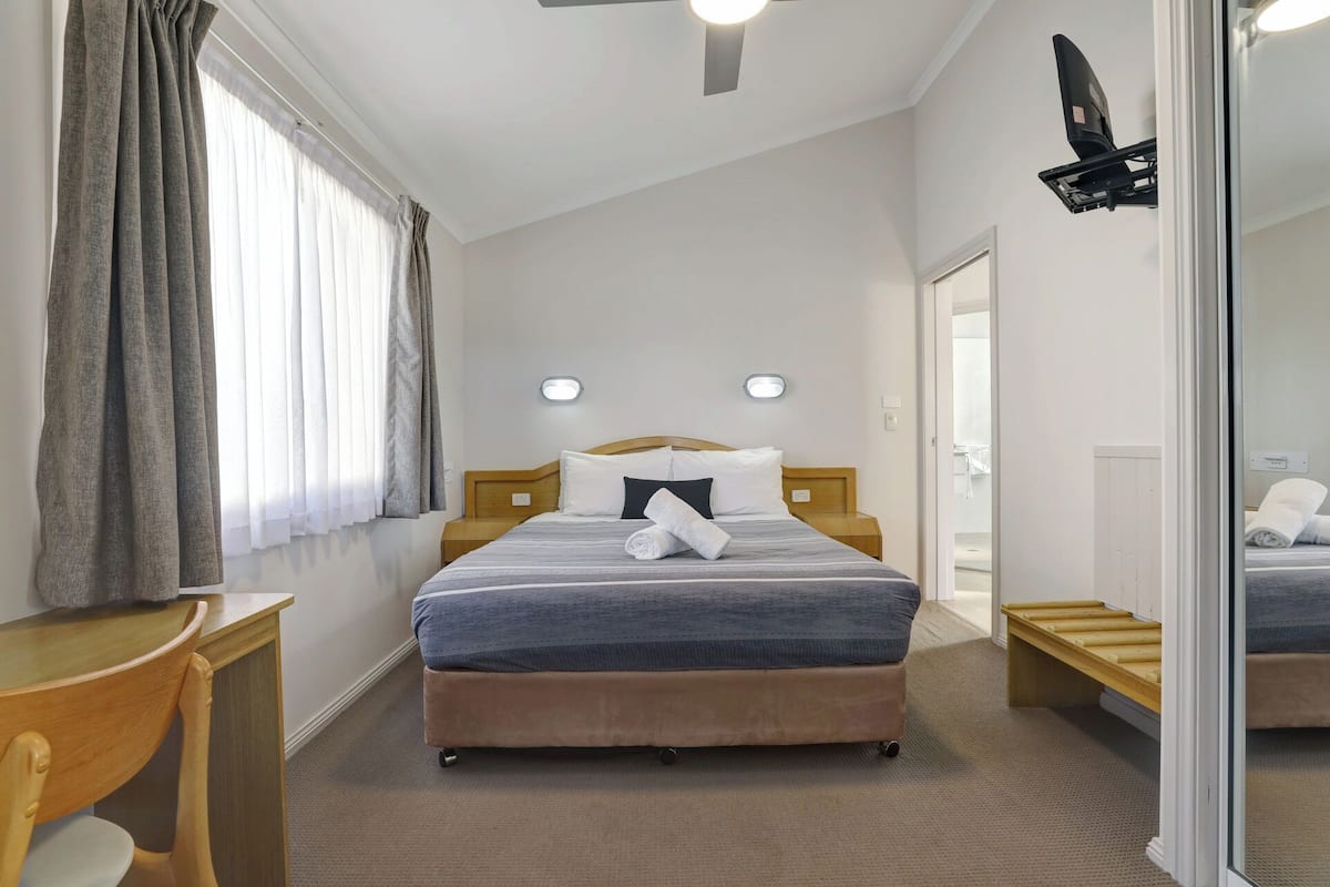 A hotel room with a bed, bedside tables, a desk, a chair, and a mirror.