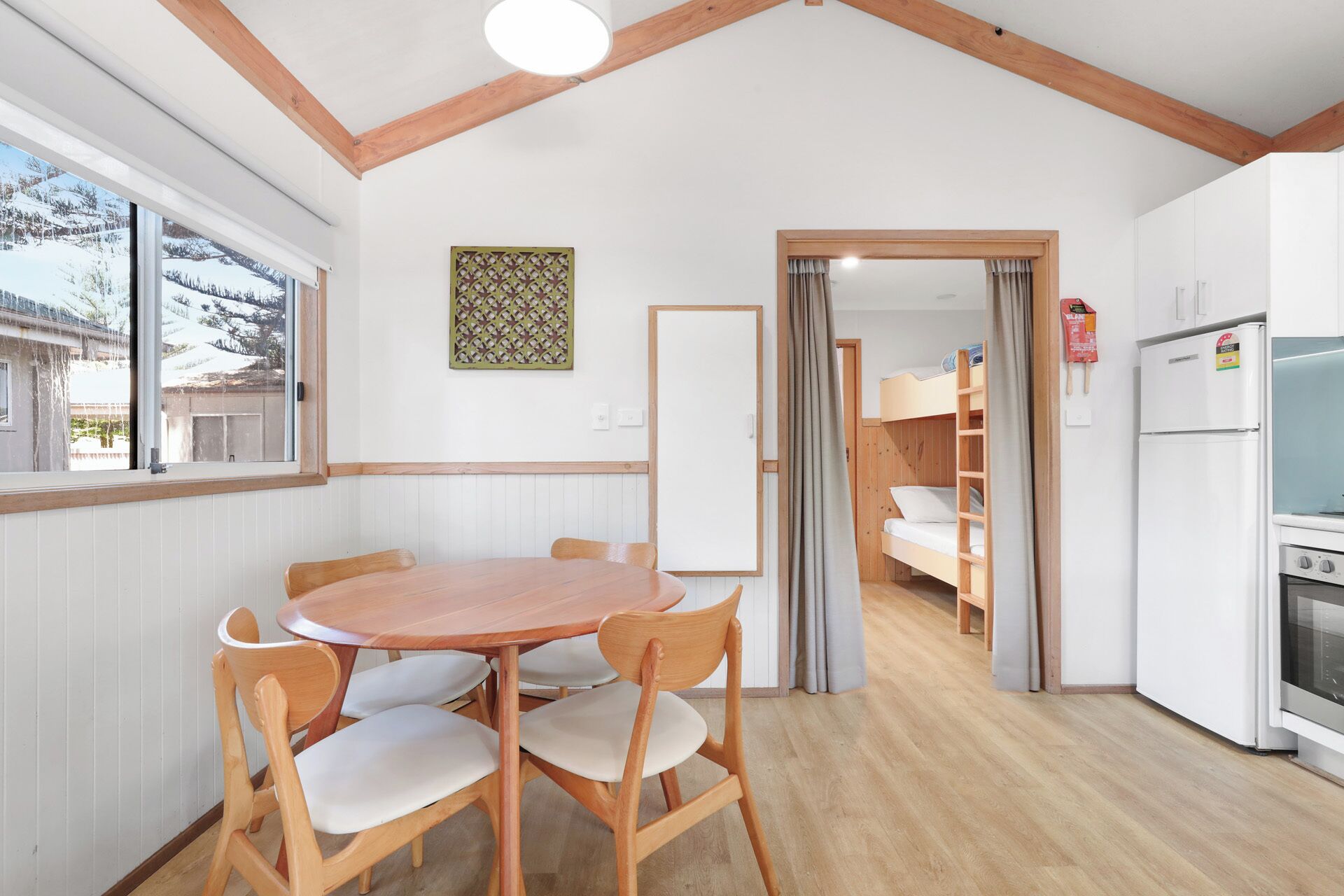 A cozy room with a wooden dining table and chairs, a white refrigerator, and a view of a snowy landscape through a large window.