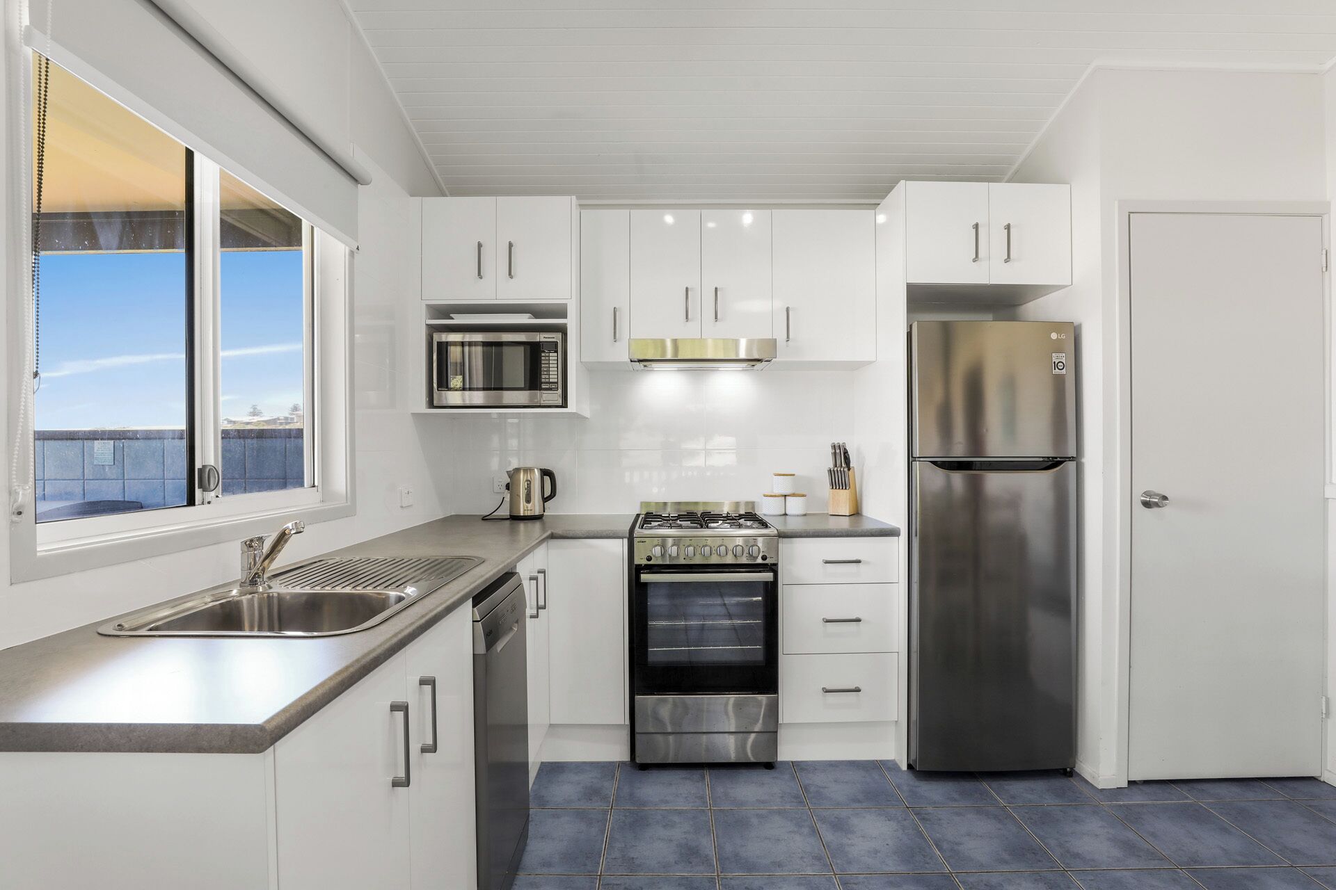 A modern kitchen with white cabinets, stainless steel appliances, a gas stove, a microwave, and a refrigerator.