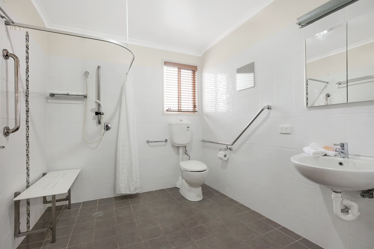 A bathroom with a shower, toilet, and sink, equipped with grab bars and a window.