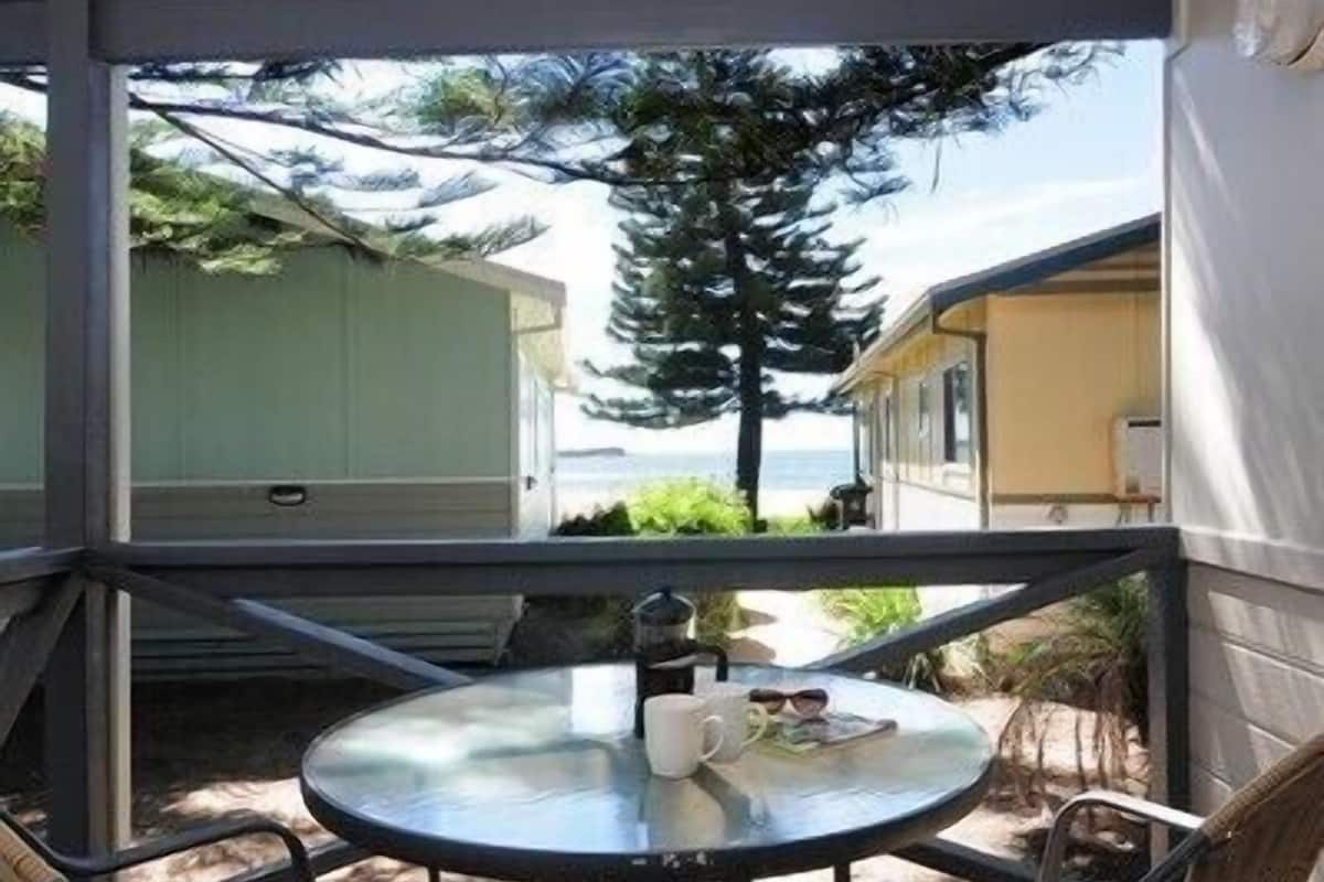 A covered outdoor patio with a round table and four chairs, overlooking a residential area and the ocean.