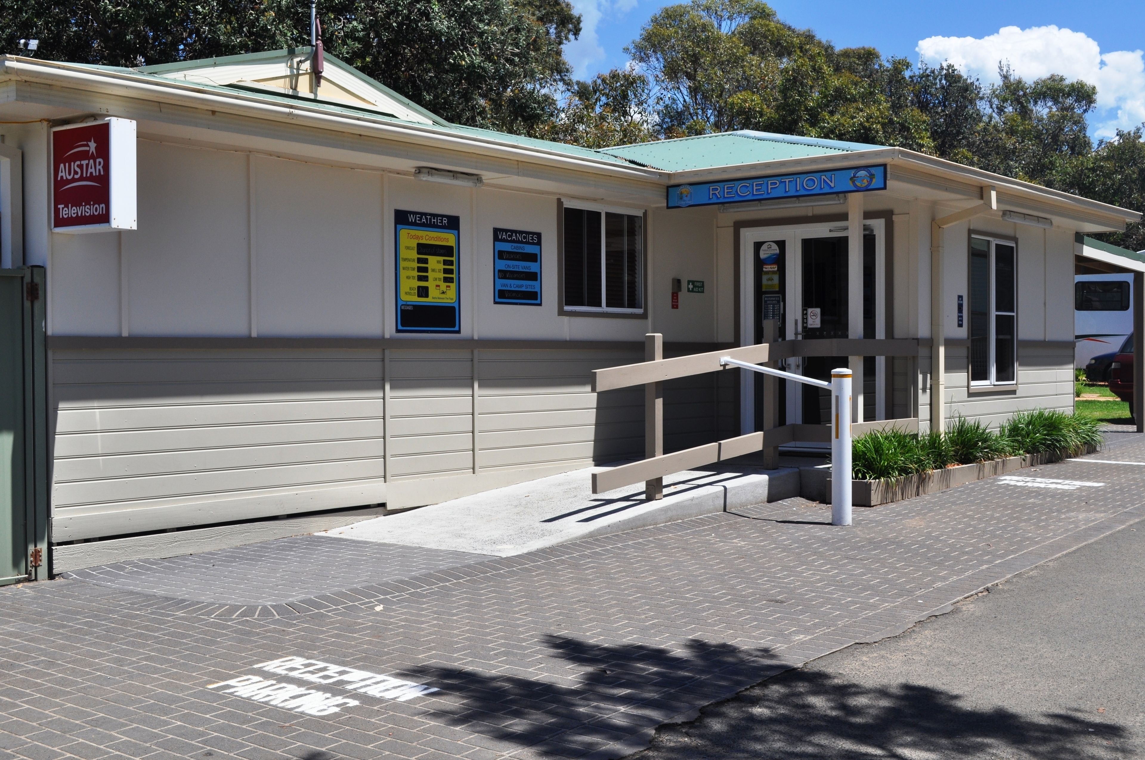 A reception area with a sign for 'Austar Television' and a 'Reception' sign above the door. There are weather and vacancies signs on the wall.