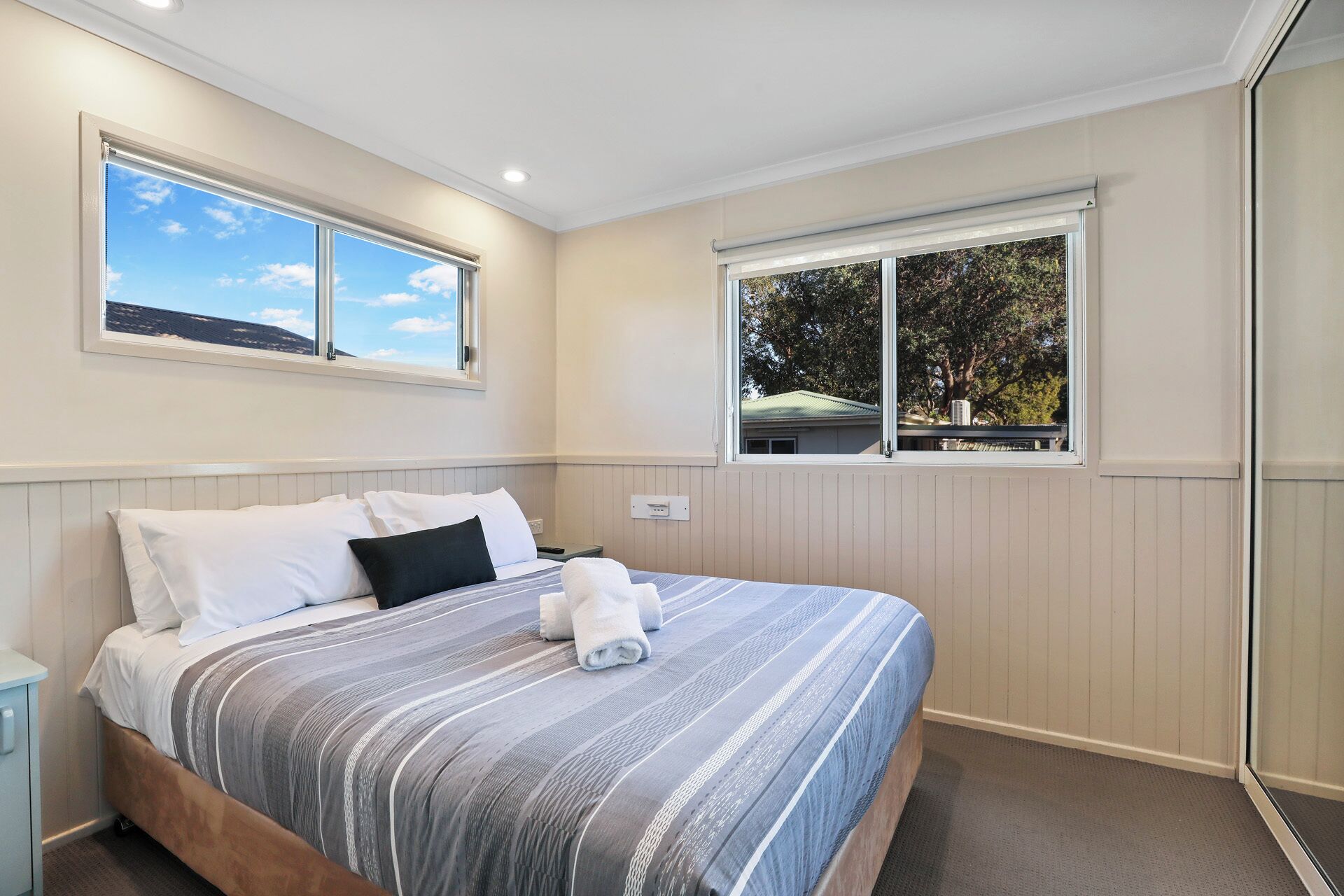Un dormitorio con cama, dos ventanas y vistas a árboles.