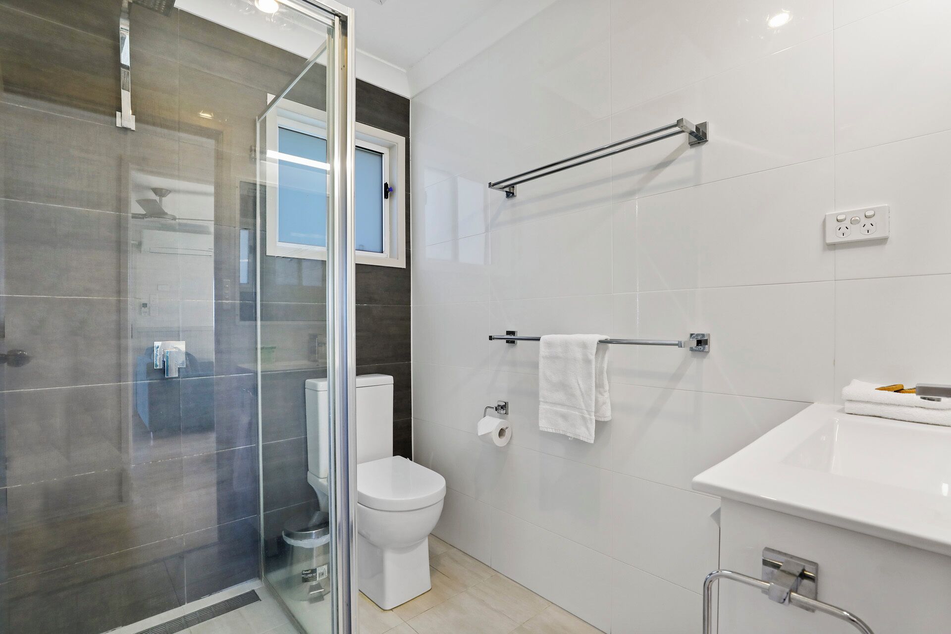 Ein modernes Badezimmer mit Duschkabine aus Glas, Toilette, Handtuchhalter und Waschbecken.