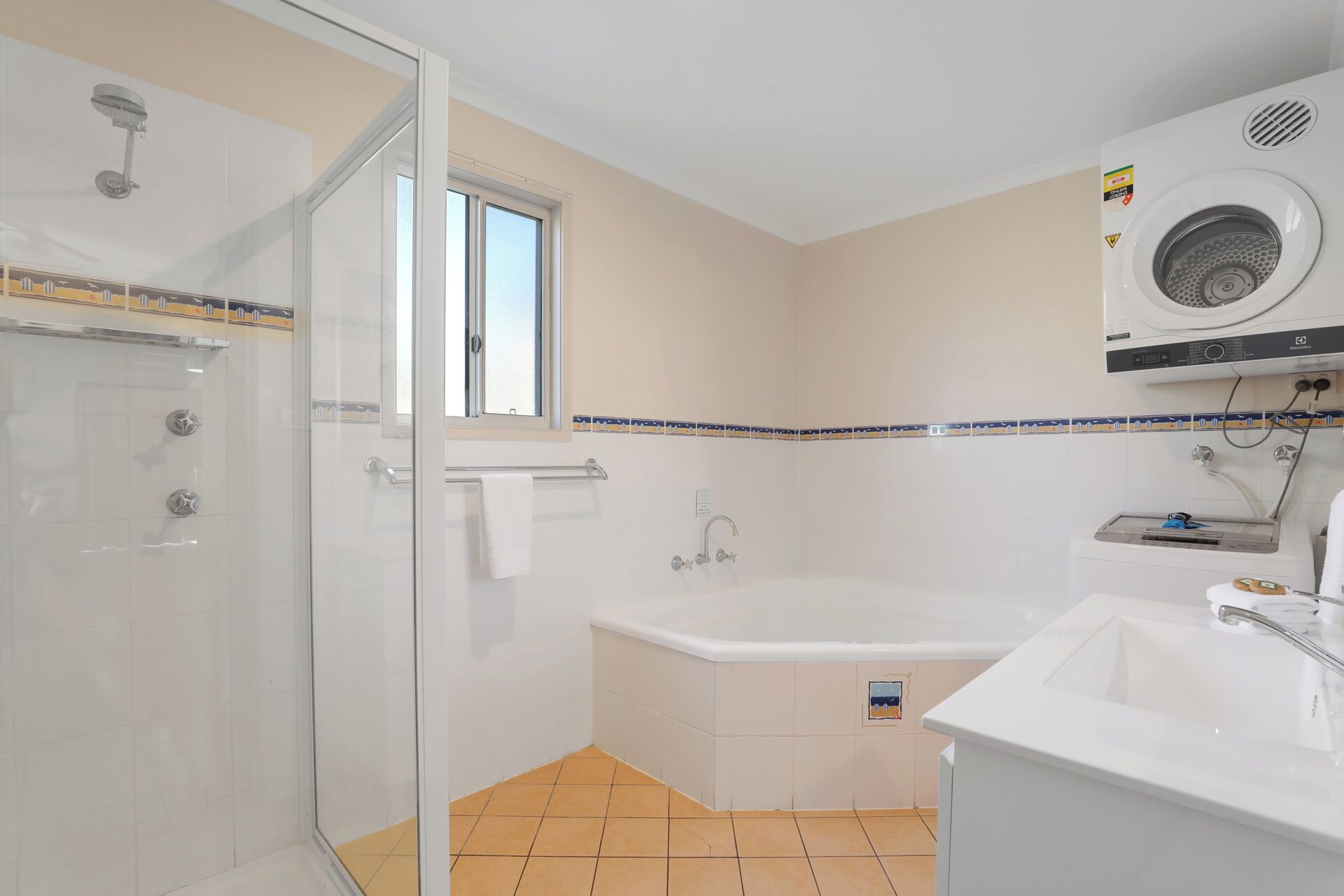A bathroom with a glass shower enclosure, a bathtub, a sink, and a window.