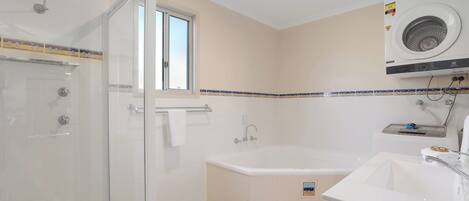 A bathroom with a glass shower enclosure, a bathtub, a sink, and a window.