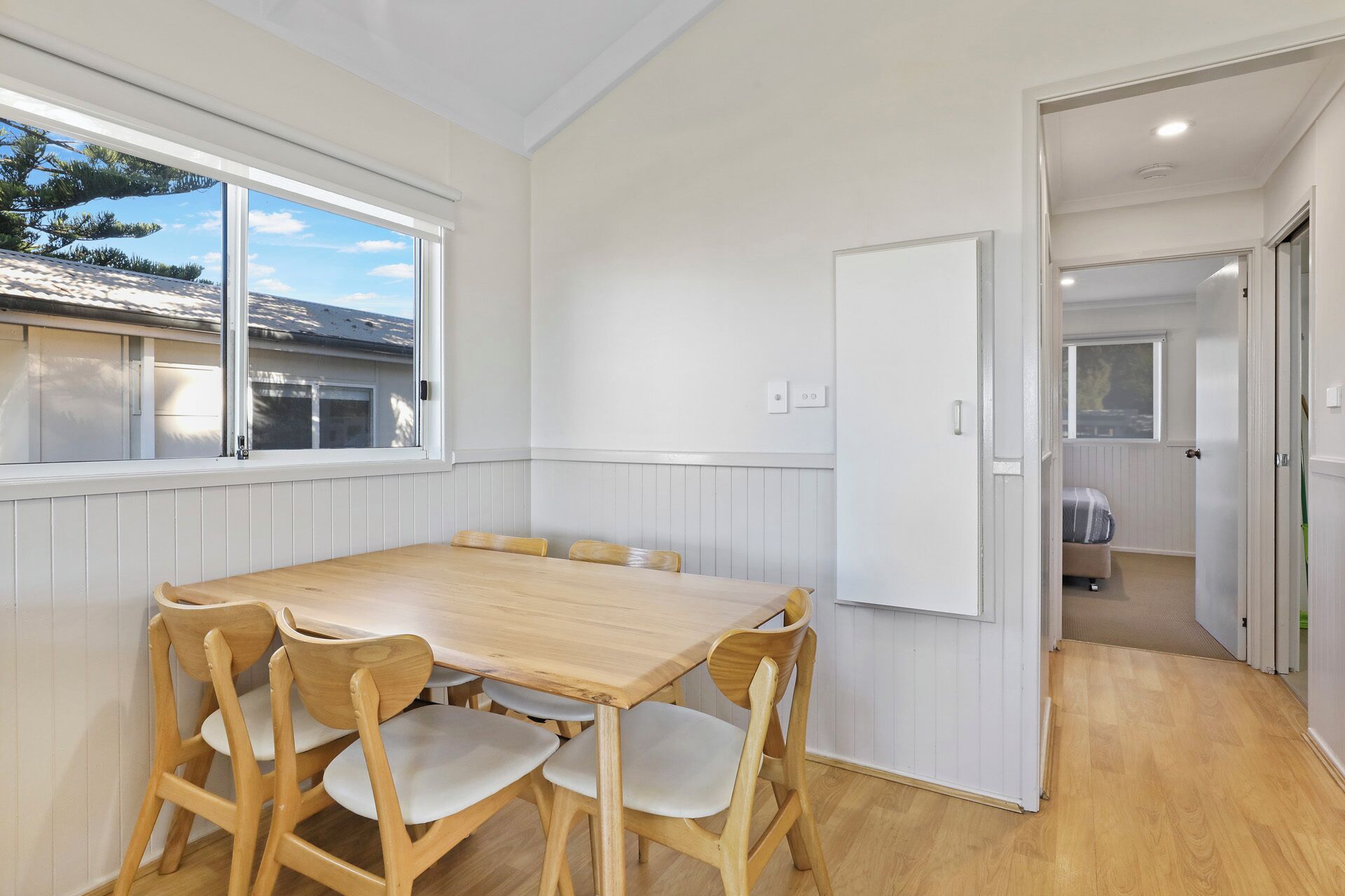 Une pièce avec une table et des chaises en bois, un tableau blanc et une vue sur l’extérieur par une fenêtre.