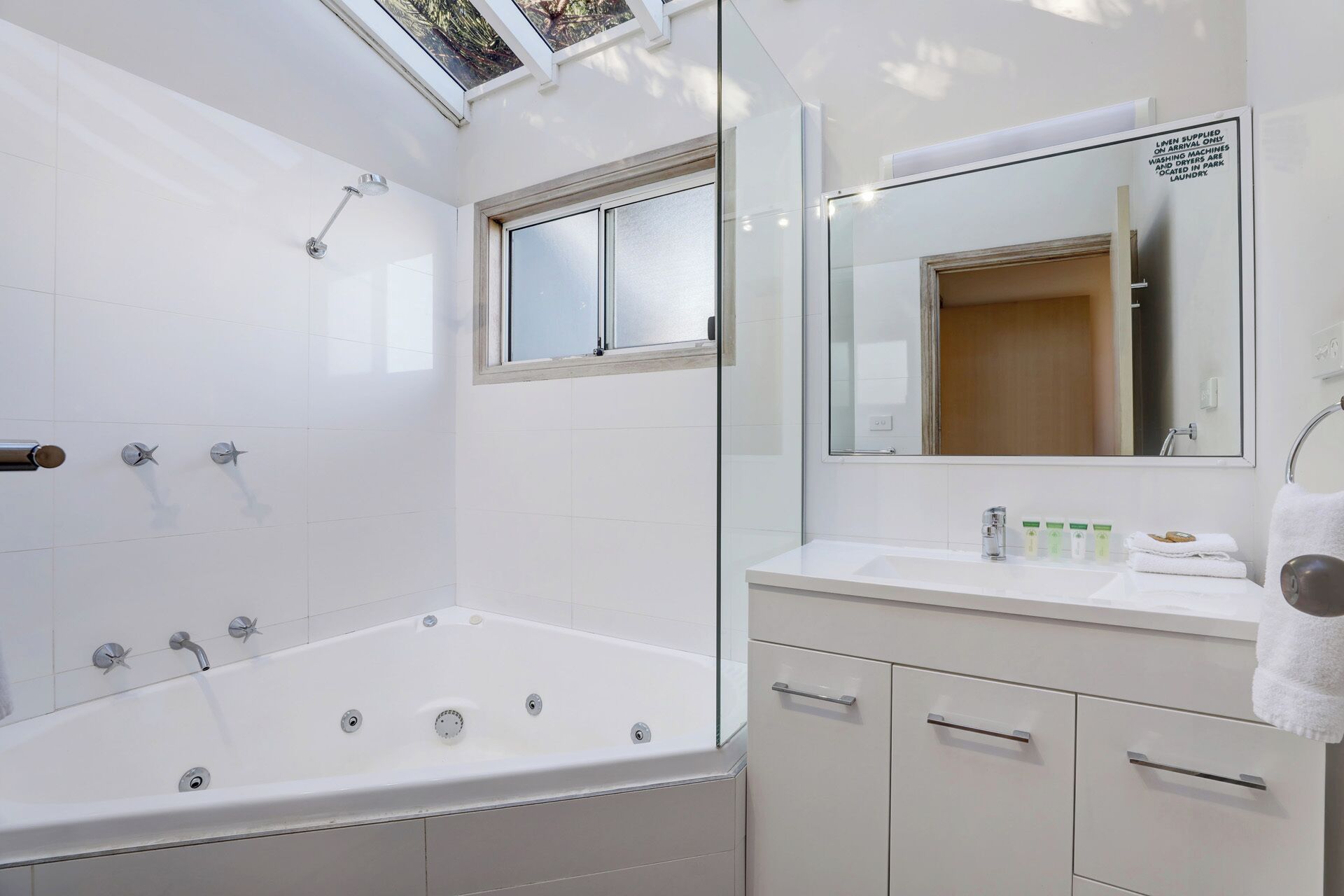 A modern bathroom with a large bathtub, a shower, a vanity with a mirror, and a window.
