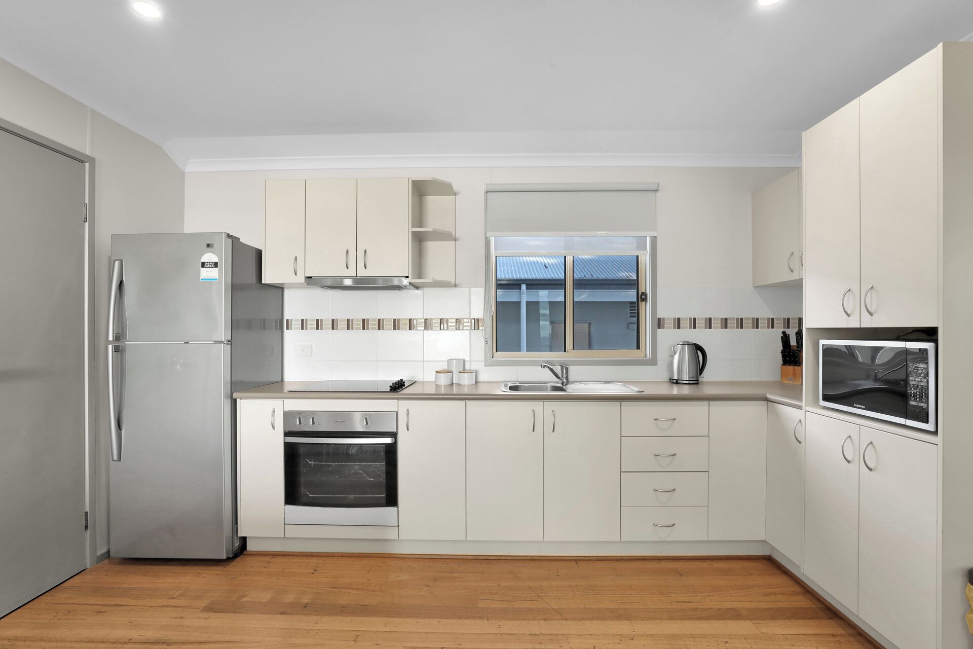 A modern kitchen with a stainless steel refrigerator, oven, and microwave, wooden flooring, and white cabinetry.