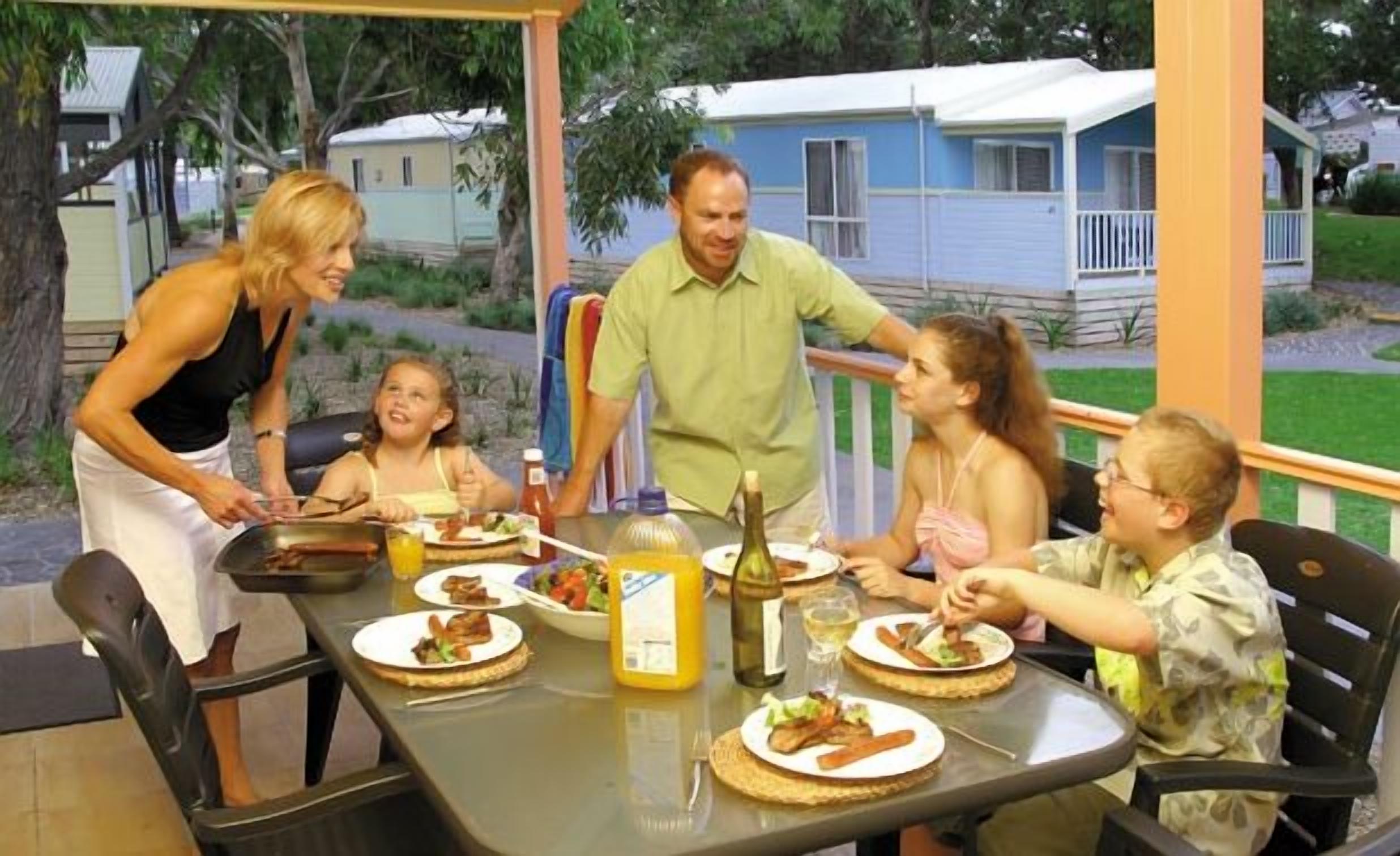 A family dining outdoors at a table with food and drinks.