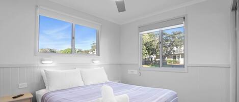 A bedroom with a bed, two windows, a ceiling fan, and a nightstand.