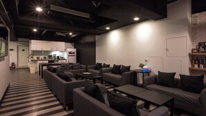 A modern lounge area with sofas, a coffee table, and a small kitchen in the background. - Fun Inn Taipei Hostel (Taipei)