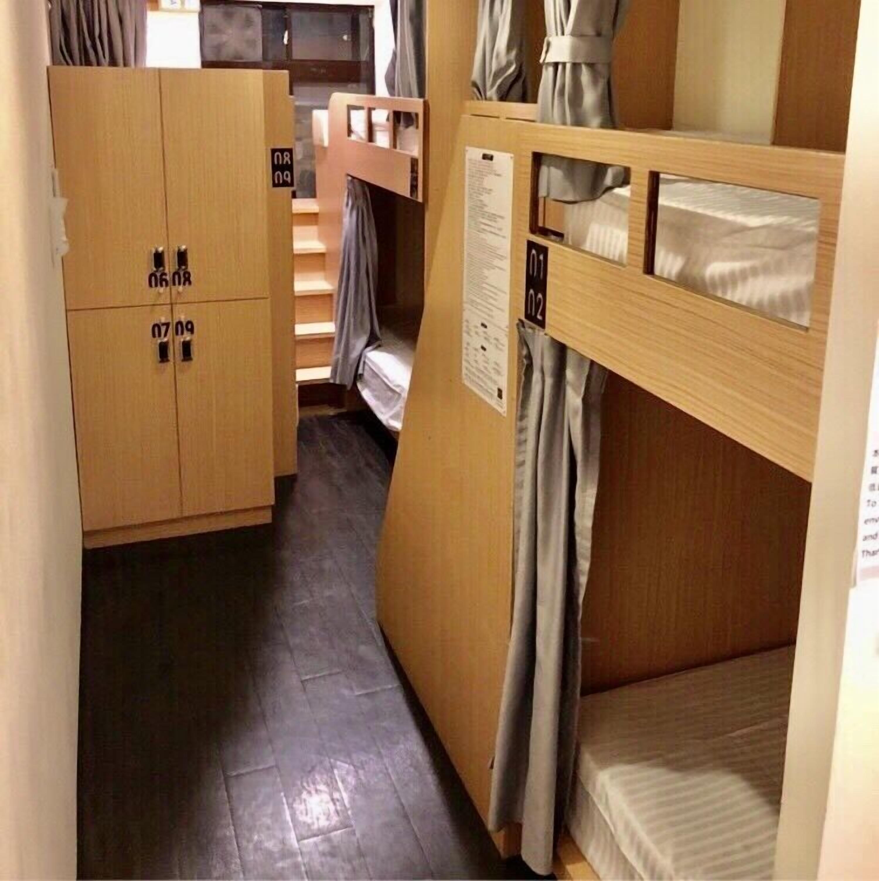A narrow corridor with wooden bunk beds on one side and a wooden wardrobe with numbered compartments on the other.