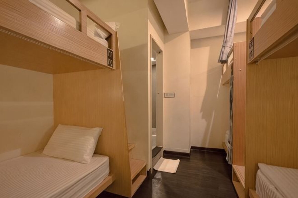 A narrow hotel corridor with bunk beds on either side, a door at the end, and a small rug on the floor.