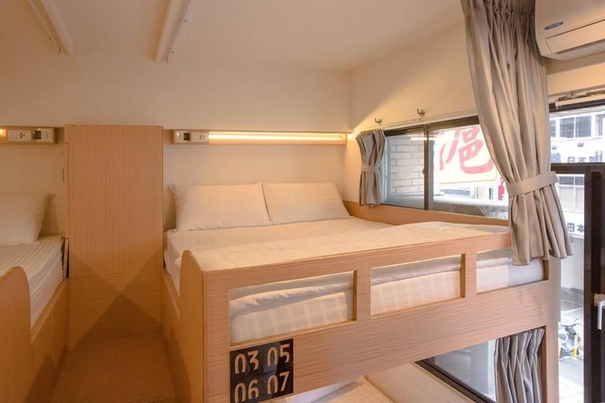 A bunk bed with a wooden frame and white bedding, a small wardrobe, and a window with curtains.
