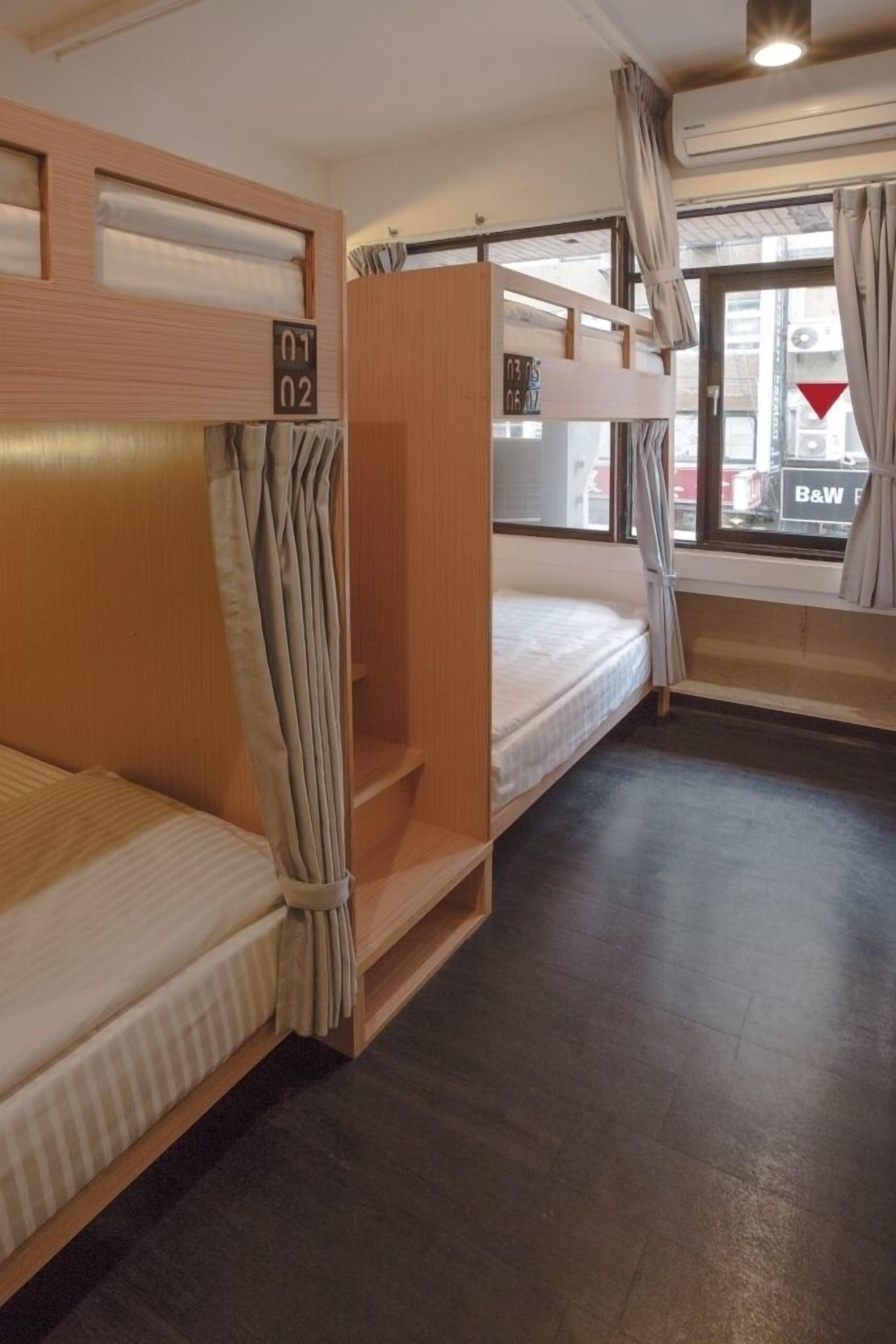 A dormitory room with bunk beds, a window with curtains, and a view of the outside.